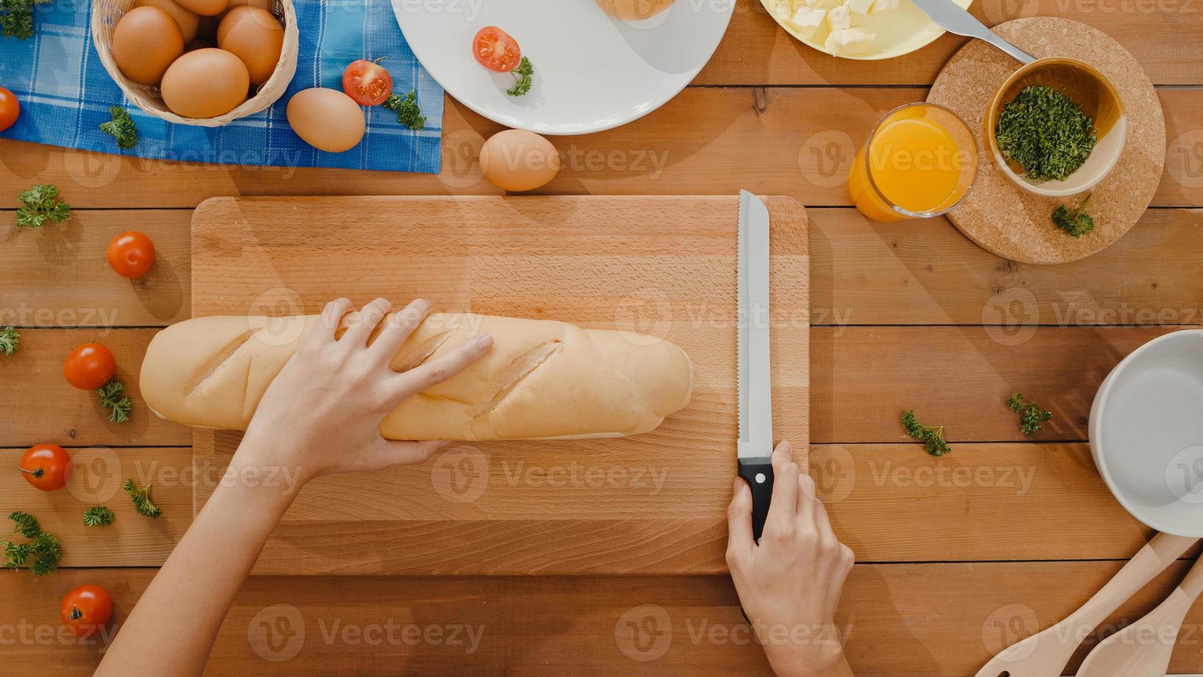 mãos do chef jovem mulher asiática segurar faca cortar pão integral na placa de madeira na mesa da cozinha em casa. produção de pão caseiro fresco, alimentação saudável e conceito tradicional de padaria. vista de cima. foto