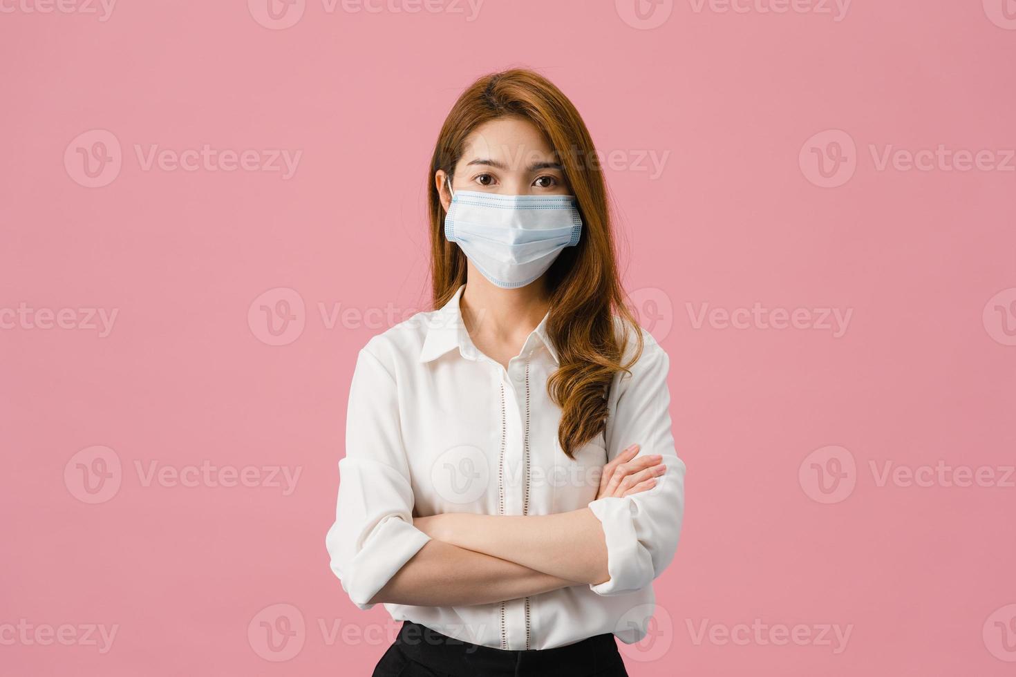 jovem asiática usando máscara médica com os braços cruzados, vestida com um pano casual e olhando para a câmera isolada sobre fundo azul. auto-isolamento, distanciamento social, quarentena para o vírus corona. foto