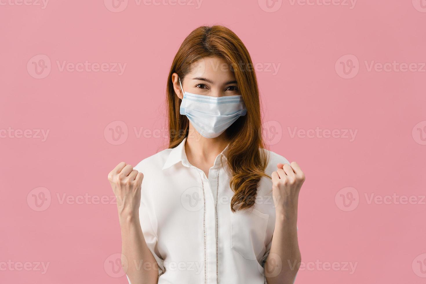 jovem asiática usando máscara médica mostrando o símbolo da paz, incentive com vestido de pano casual e olhando para a câmera isolada no fundo rosa. distanciamento social, quarentena para o vírus corona. foto