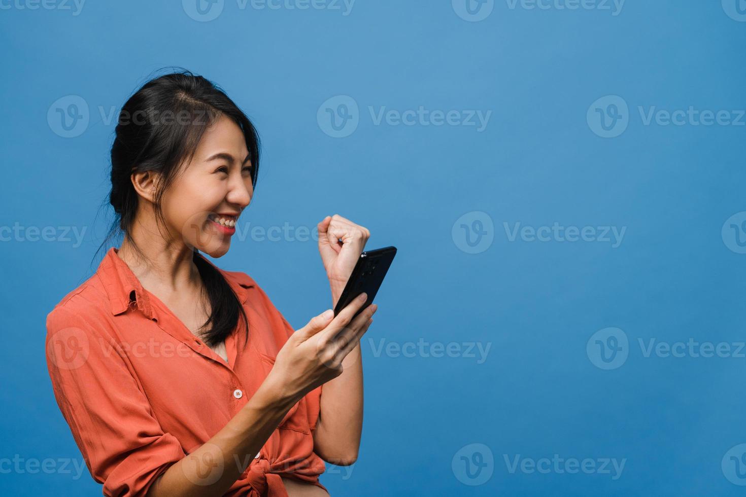 surpreendeu a jovem asiática usando telefone celular com expressão positiva, sorri amplamente, vestida com roupas casuais e carrinho isolado sobre fundo azul. feliz adorável feliz mulher alegra sucesso. foto