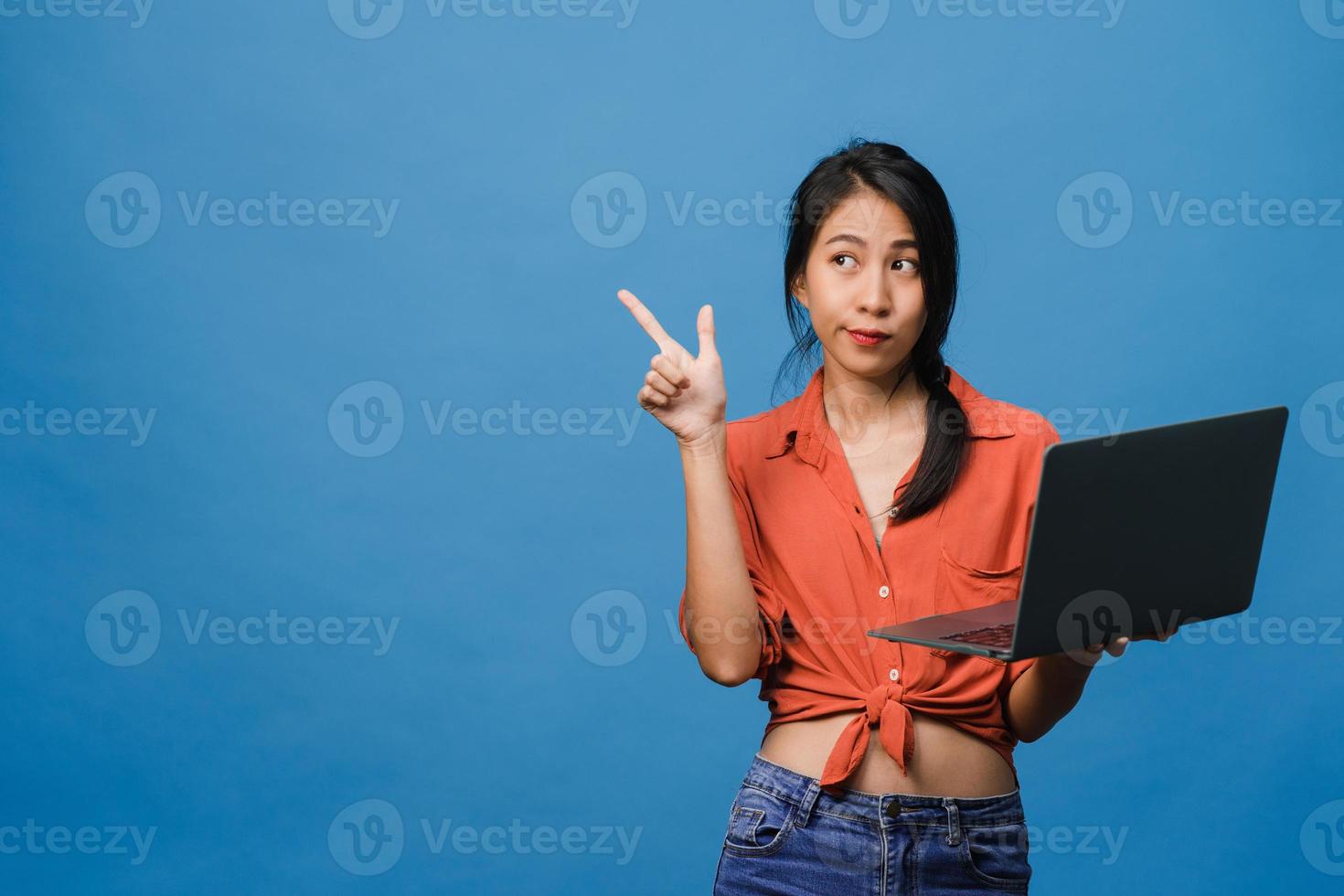 jovem asiática usando laptop com expressão positiva, sorri amplamente, vestida com roupas casuais, sentindo felicidade e carrinho isolado sobre fundo azul. feliz adorável feliz mulher alegra sucesso. foto