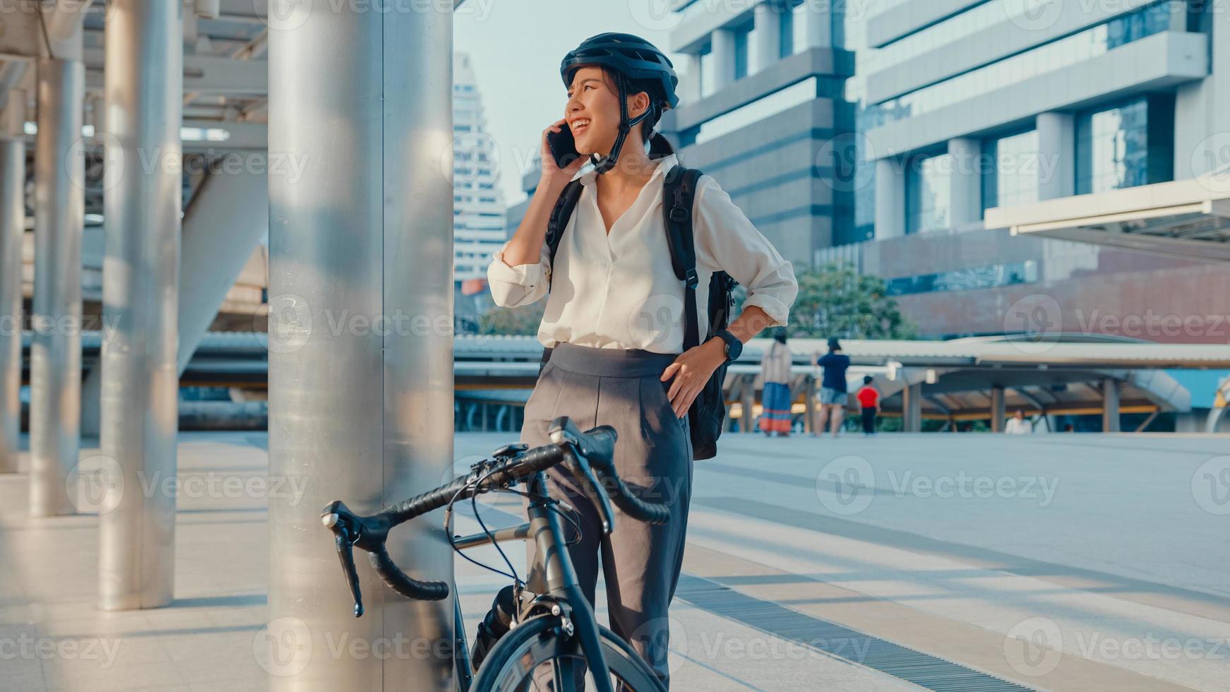 empresária asiática com mochila pegar conversa de celular sorrindo smartwatch relógio na rua da cidade ir trabalhar no escritório. menina do esporte usa o negócio do telefone. comuta para o trabalho de bicicleta, viajante de negócios na cidade. foto