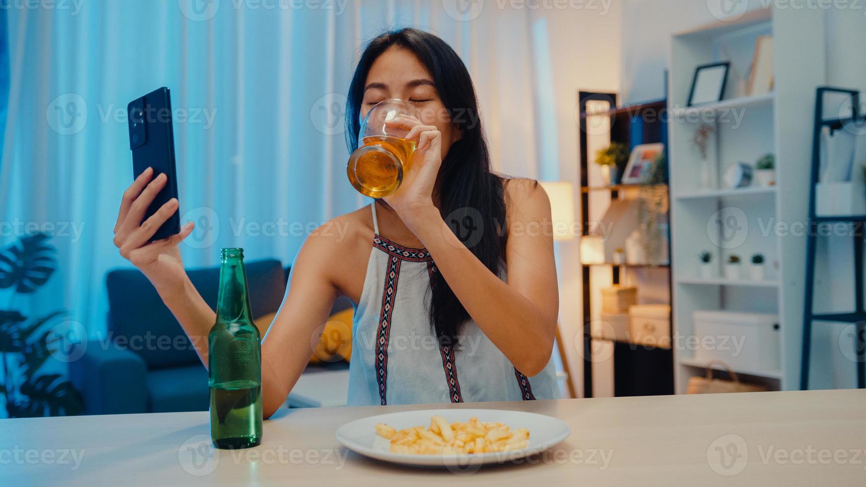 jovem asiática bebendo cerveja se divertindo momento feliz noite festa ano novo evento on-line celebração via videochamada por telefone em casa à noite. distanciamento social, quarentena para prevenção de coronavírus. foto