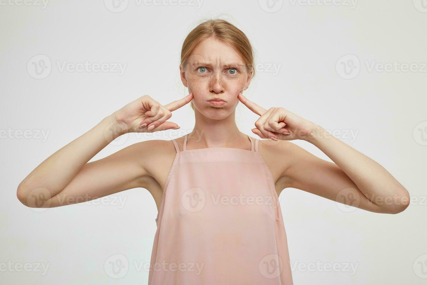 interior foto do jovem atraente ruiva senhora bufando Fora dela bochechas e guardando elevado indicadores em isto, enganar enquanto em pé sobre branco fundo