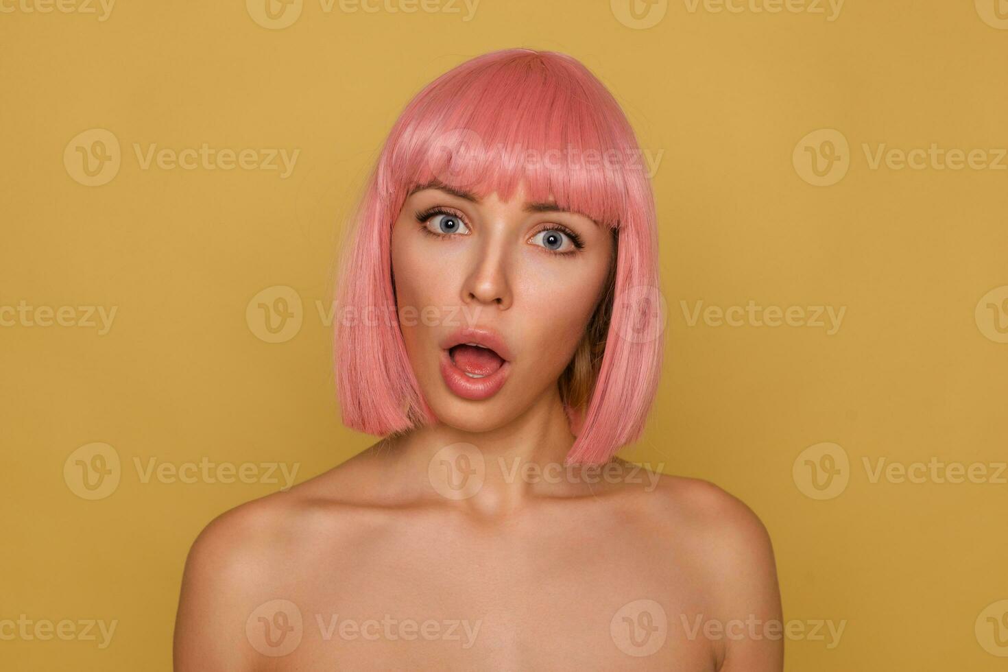 estúdio foto do confuso jovem bonita senhora com curto Rosa cabelo guardando dela boca aberto enquanto olhando perplexo às Câmera, em pé contra mostarda fundo