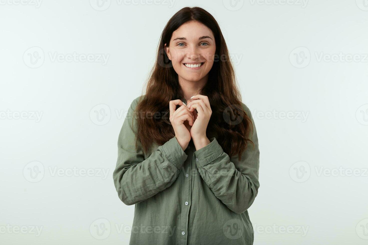 satisfeito jovem encantador morena fêmea com natural Maquiagem olhando alegremente às Câmera com amplo sorrir e dobrando elevado mãos enquanto posando sobre branco fundo foto