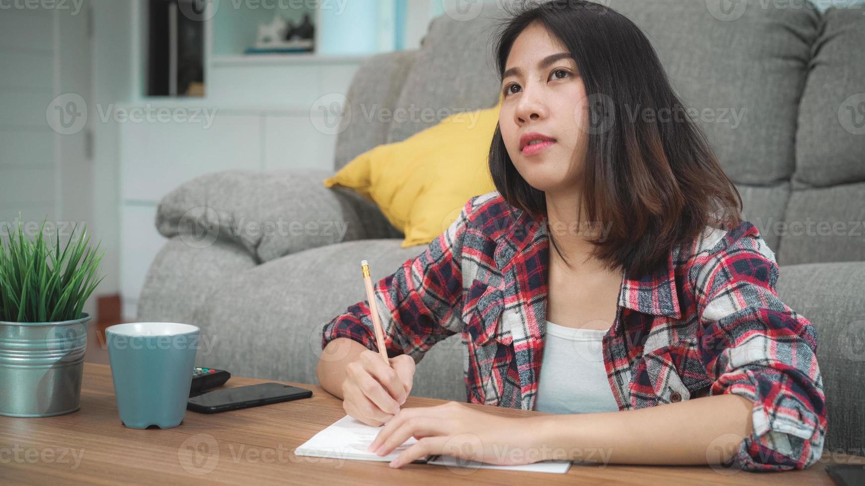 mulher estudante asiática fazer lição de casa em casa, mulher usando tablet para pesquisar no sofá na sala de estar em casa. mulheres de estilo de vida relaxam no conceito de casa. foto