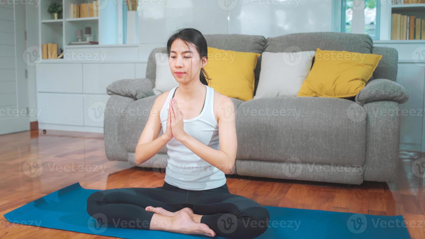 jovem mulher asiática praticando ioga na sala de estar. atraente mulher bonita malhando para uma saúde saudável em casa. conceito de exercício de mulher de estilo de vida. foto