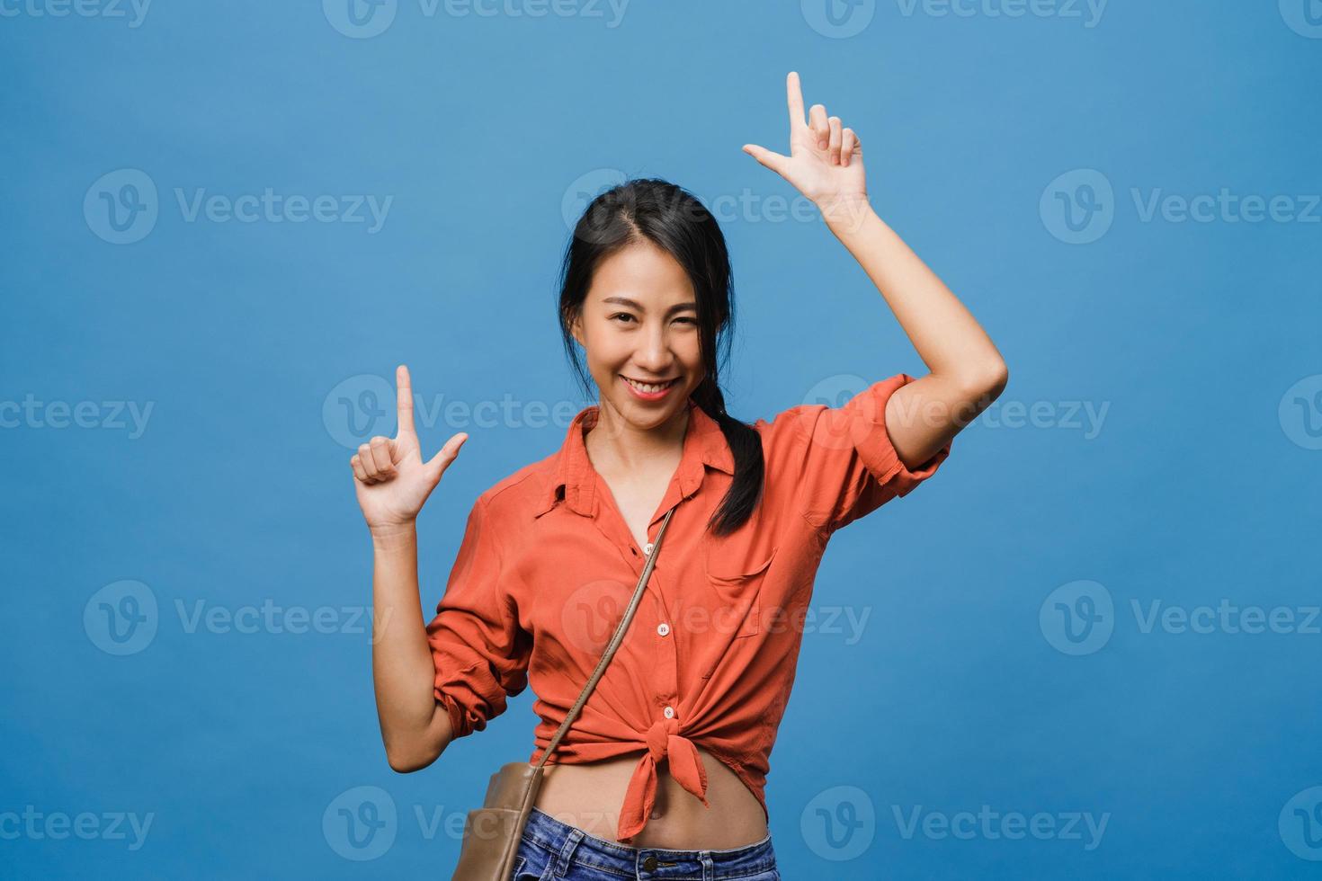 retrato de uma jovem asiática sorrindo com uma expressão alegre, mostra algo incrível no espaço em branco em um pano casual e olhando para a câmera isolada sobre fundo azul. conceito de expressão facial. foto