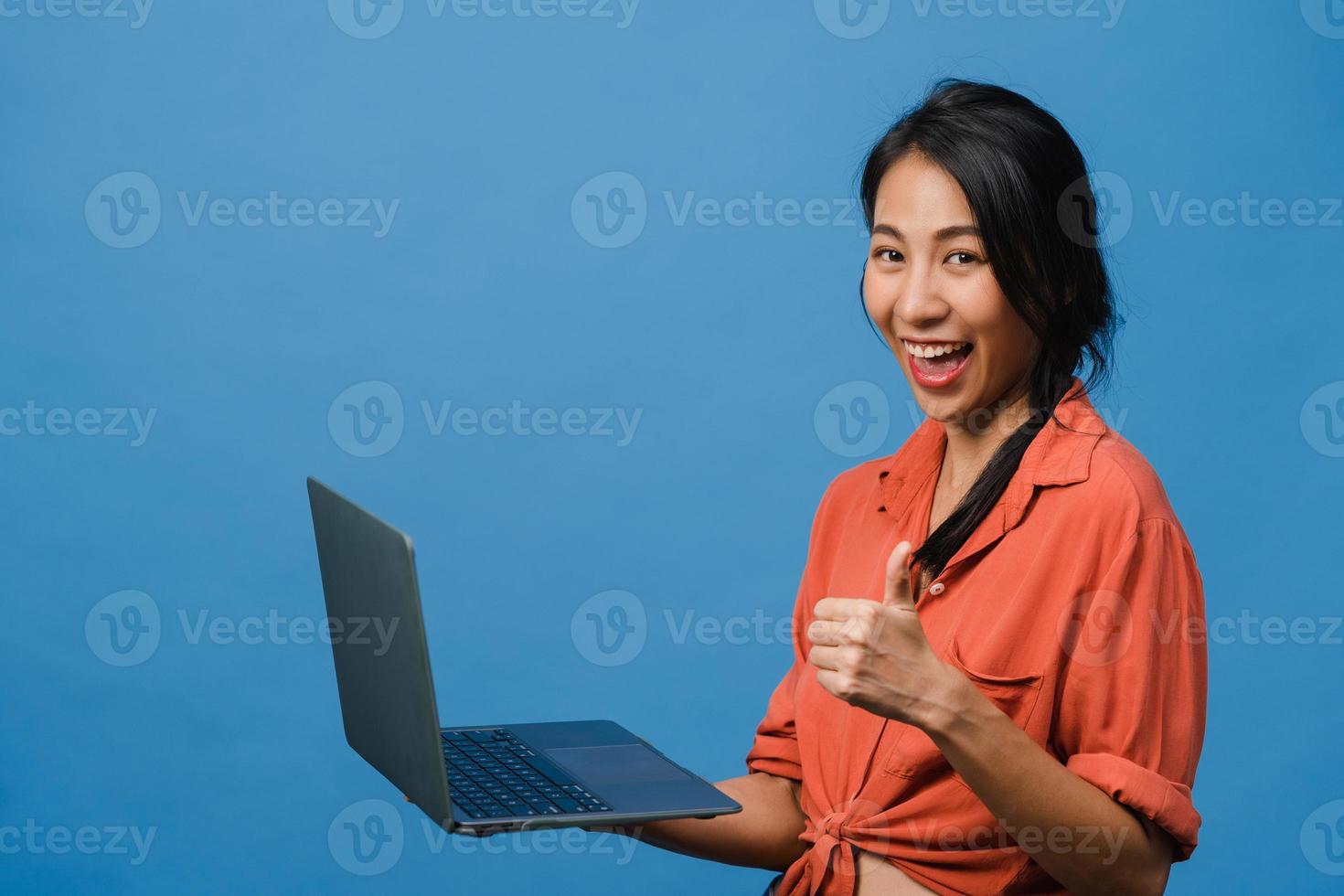 jovem asiática usando laptop com expressão positiva, sorri amplamente, vestida com roupas casuais, sentindo felicidade e carrinho isolado sobre fundo azul. feliz adorável feliz mulher alegra sucesso. foto