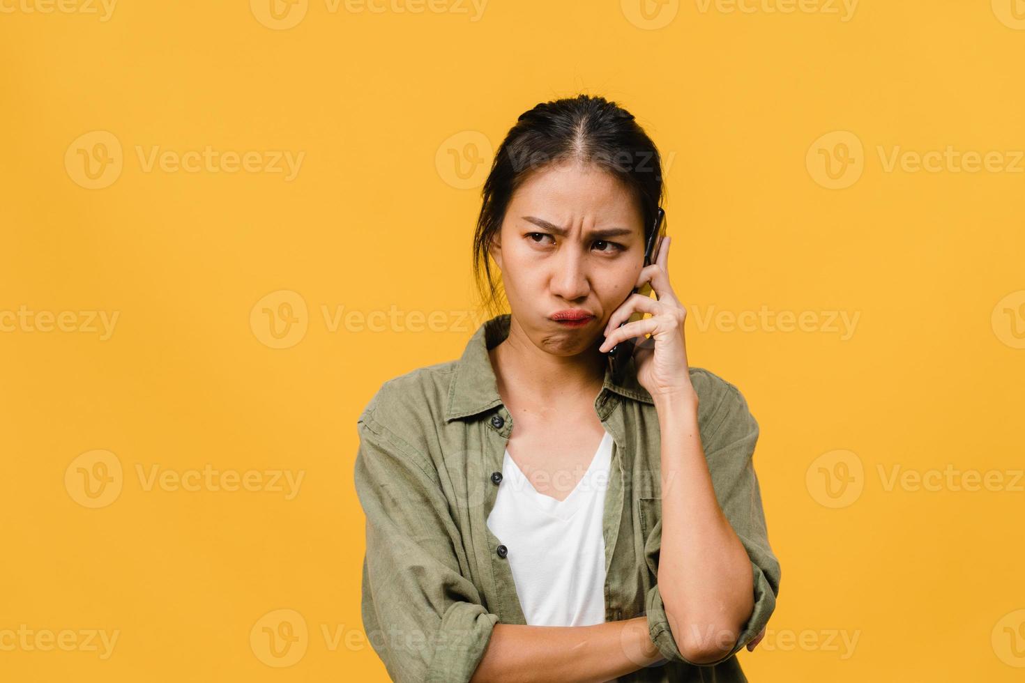 jovem asiática fala por telefone com expressão negativa, gritando animado, chora com raiva emocional em um pano casual e fica isolado em um fundo amarelo com espaço de cópia em branco. conceito de expressão facial. foto