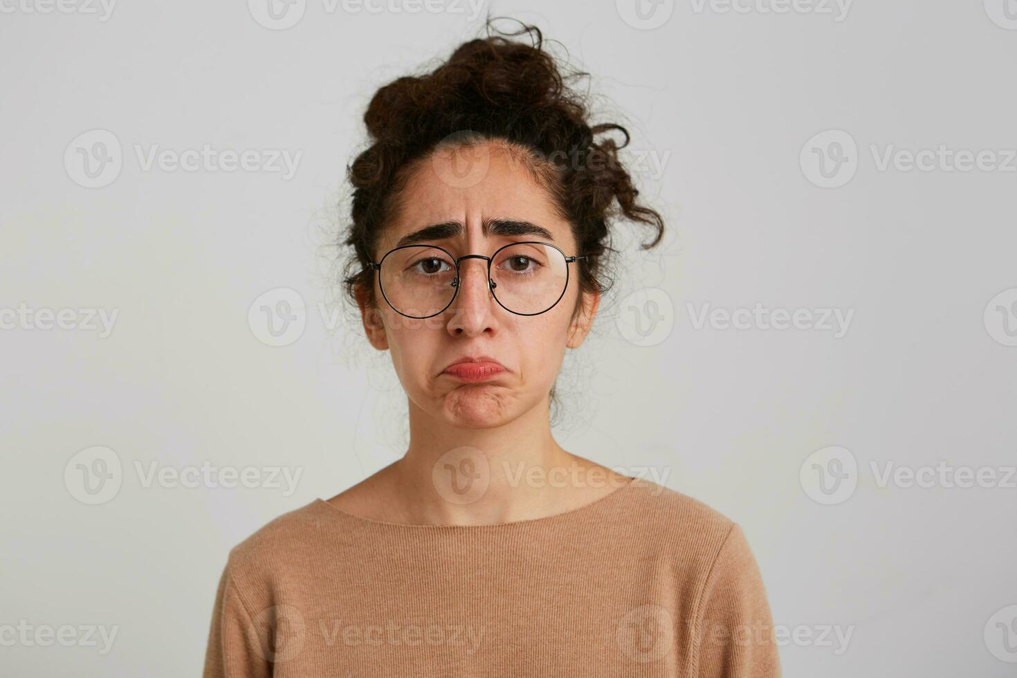 retrato do infeliz desapontado georgiano jovem mulher com encaracolado cabelo desgasta bege estacionar e óculos sente triste e depressivo isolado sobre branco fundo foto