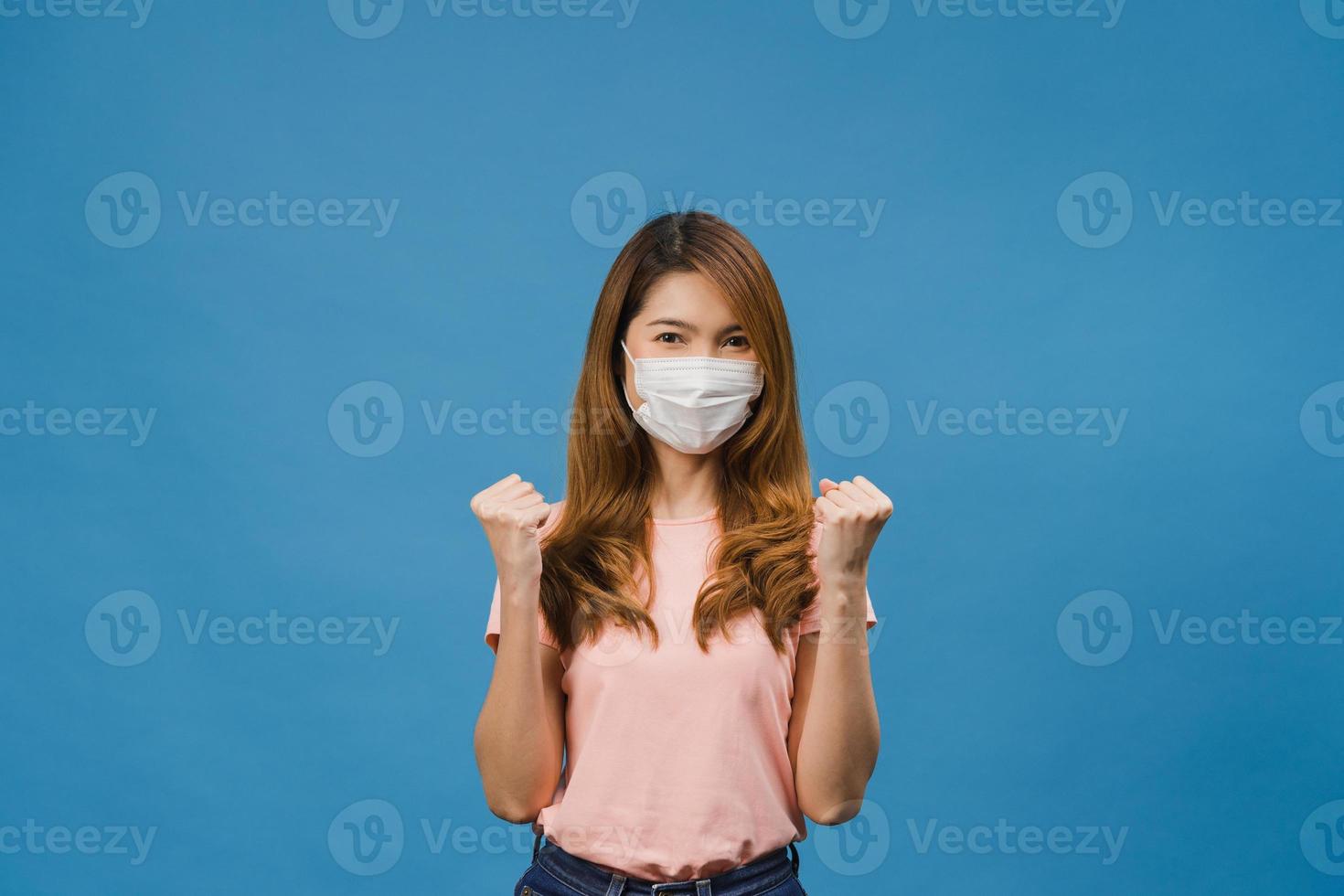 jovem asiática usando máscara médica mostrando o símbolo da paz, incentive com vestido de pano casual e olhando para a câmera isolada sobre fundo azul. distanciamento social, quarentena para o vírus corona. foto