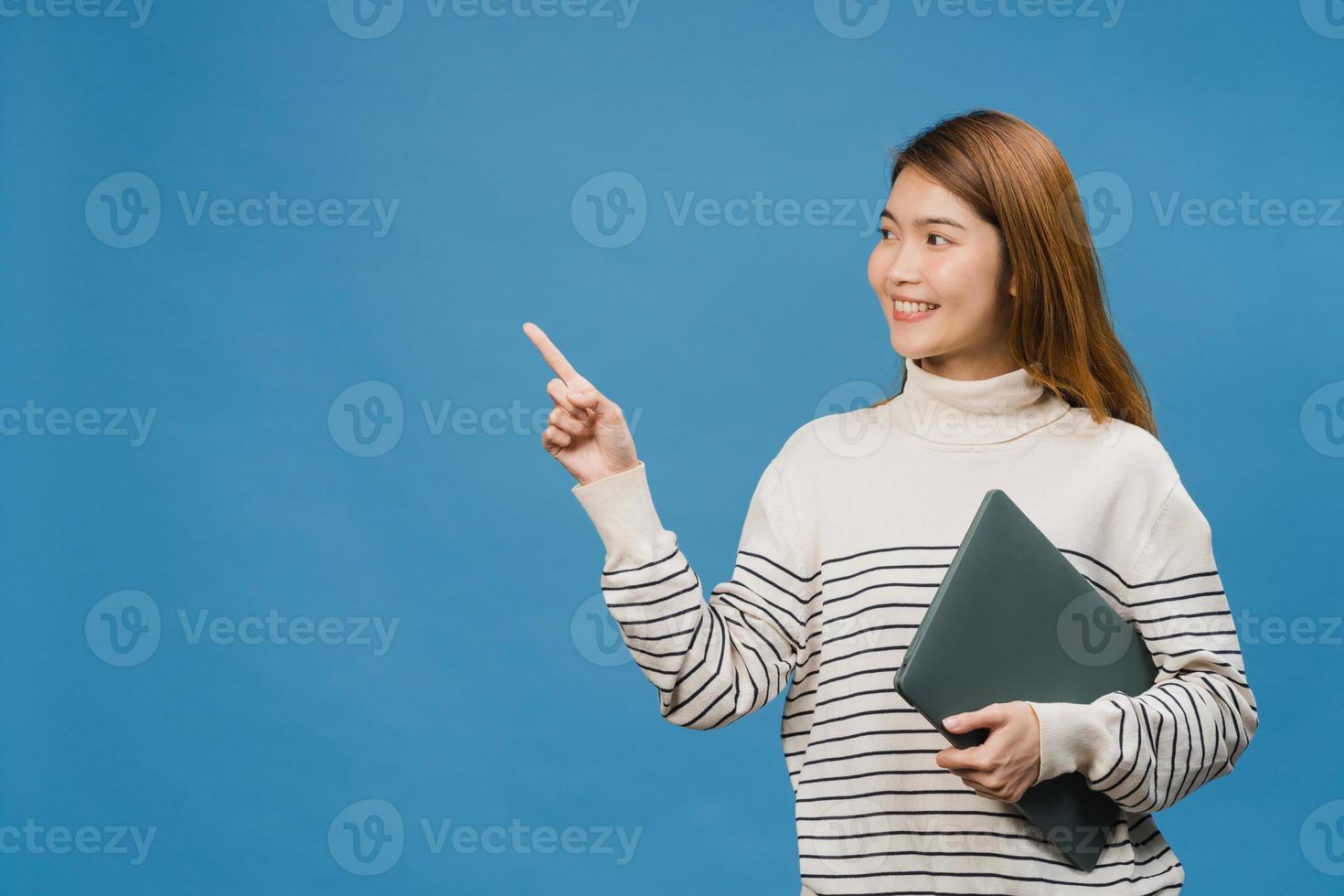 jovem asiática usando laptop com expressão positiva, sorri amplamente, vestida com roupas casuais, sentindo felicidade e carrinho isolado sobre fundo azul. feliz adorável feliz mulher alegra sucesso. foto