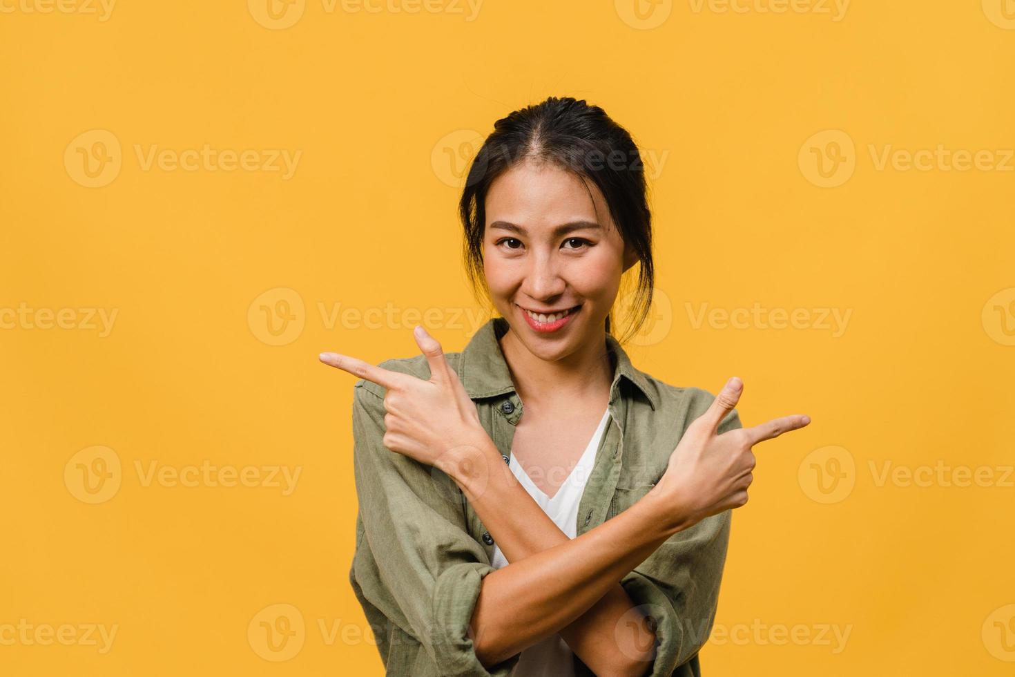 retrato de uma jovem asiática sorrindo com uma expressão alegre, mostra algo incrível no espaço em branco em um pano casual e olhando para a câmera isolada sobre fundo amarelo. conceito de expressão facial. foto