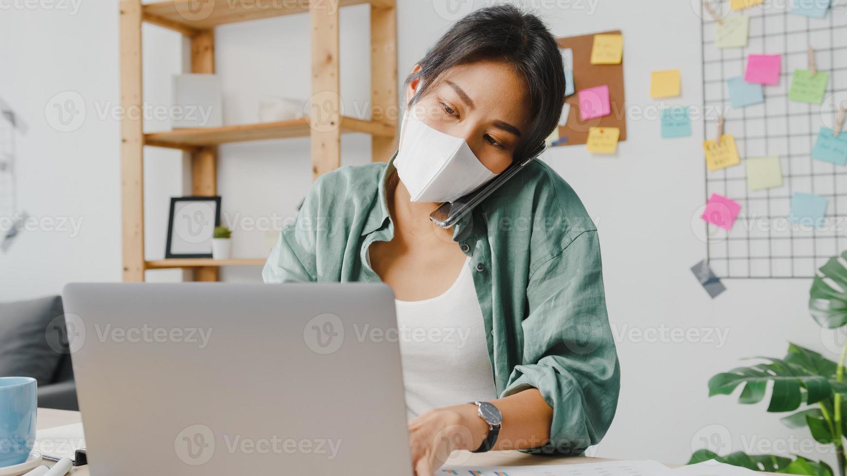 mulheres jovens asiáticas usam máscara médica falando no telefone ocupado empresário trabalhando distante na sala de estar. trabalho de casa, trabalho remoto, distanciamento social, quarentena para prevenção do vírus corona foto