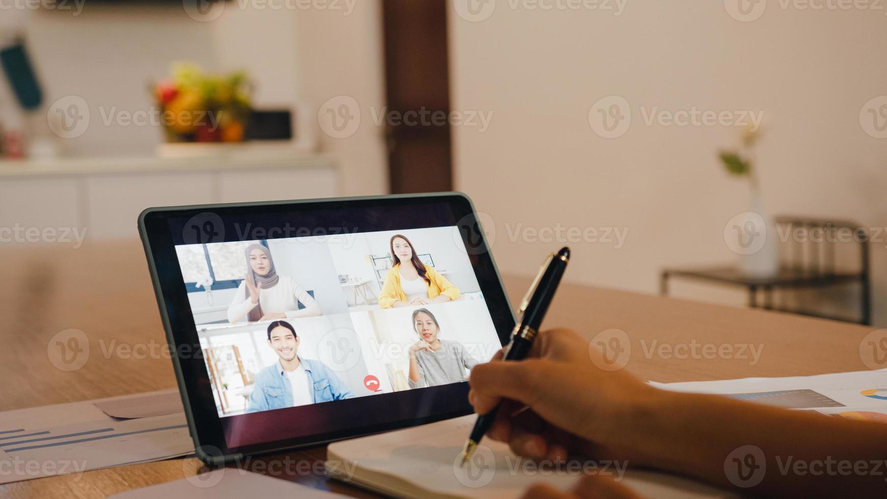 empresária asiática usando tablet digital conversa com um colega sobre plano por videochamada brainstorm reunião on-line enquanto trabalha remotamente de casa na cozinha. distanciamento social, quarentena para o vírus corona. foto