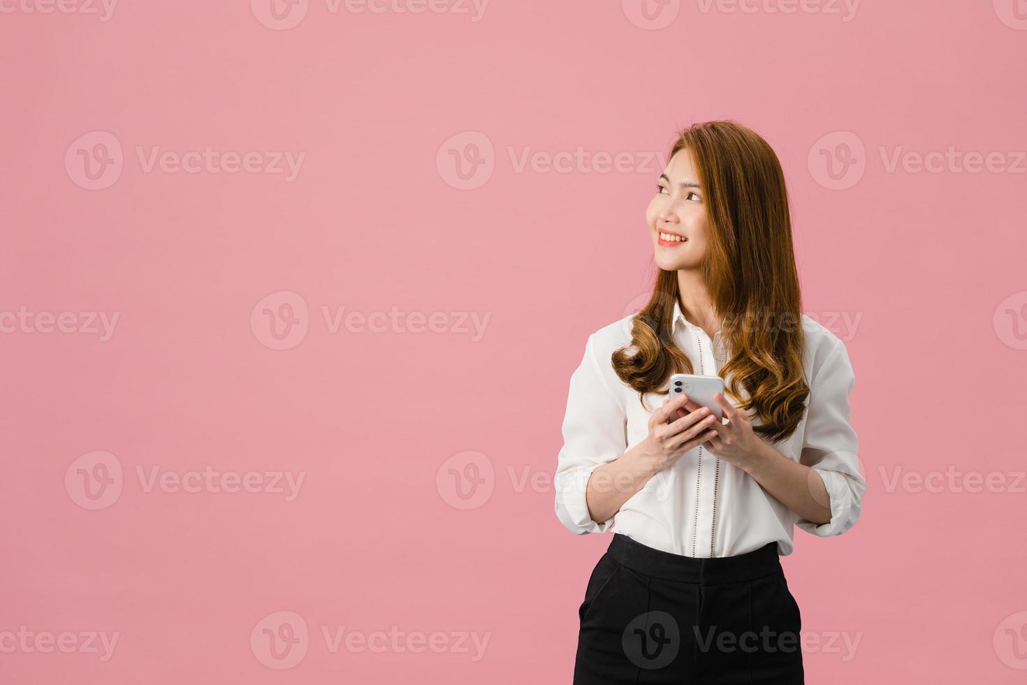 jovem asiática usando telefone com expressão positiva, sorri amplamente, vestida com roupas casuais, sentindo felicidade e estando isolada no fundo rosa. feliz adorável feliz mulher alegra sucesso. foto