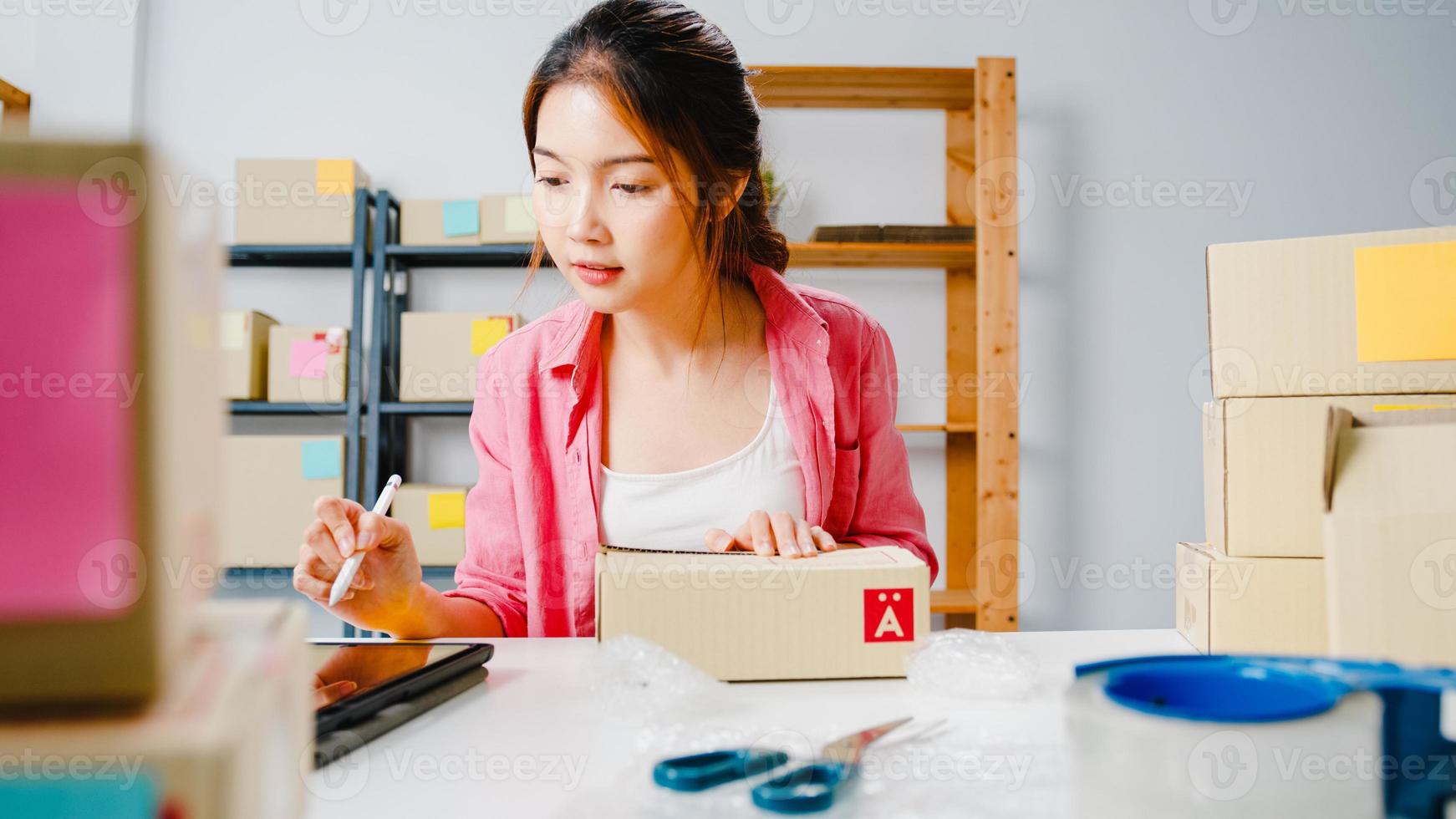 jovem ásia empresário empresária verificar o pedido de compra do produto em estoque e salvar no trabalho do computador tablet no escritório em casa. proprietário de uma pequena empresa, entrega de mercado online, conceito freelance de estilo de vida. foto