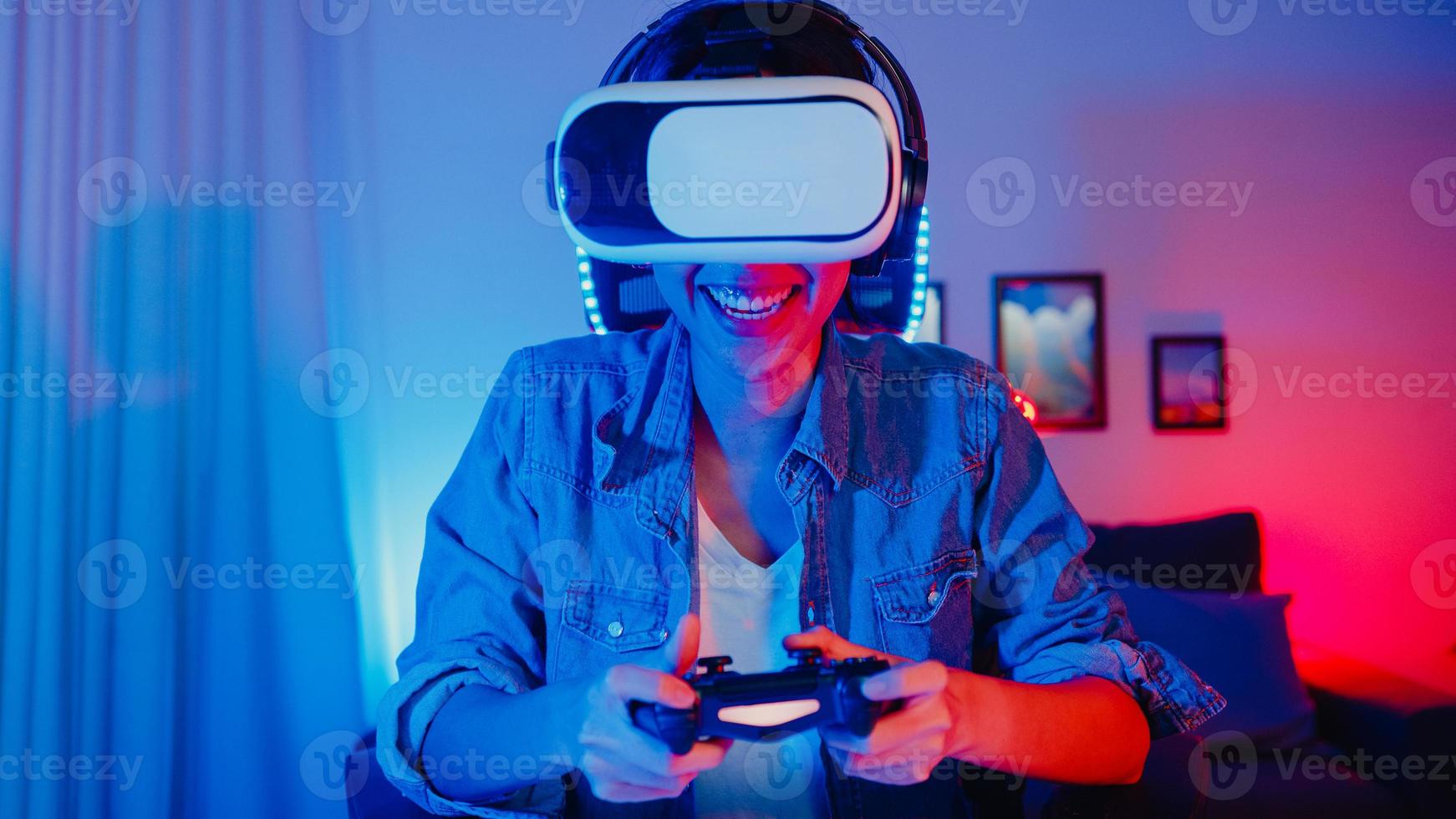 O vencedor do jogador jovem feliz da Ásia usa óculos de realidade virtual, óculos de proteção, fone de ouvido e controlador de joystick divertido e animado com o jogo online no estúdio doméstico de néon à noite, atividade de quarentena em casa. foto