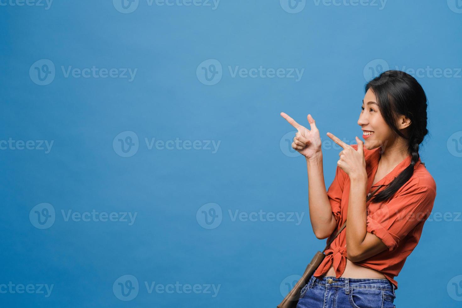 retrato de uma jovem senhora asiática, sorrindo com uma expressão alegre, mostra algo incrível no espaço em branco em roupas casuais e em pé isolado sobre um fundo azul. conceito de expressão facial. foto