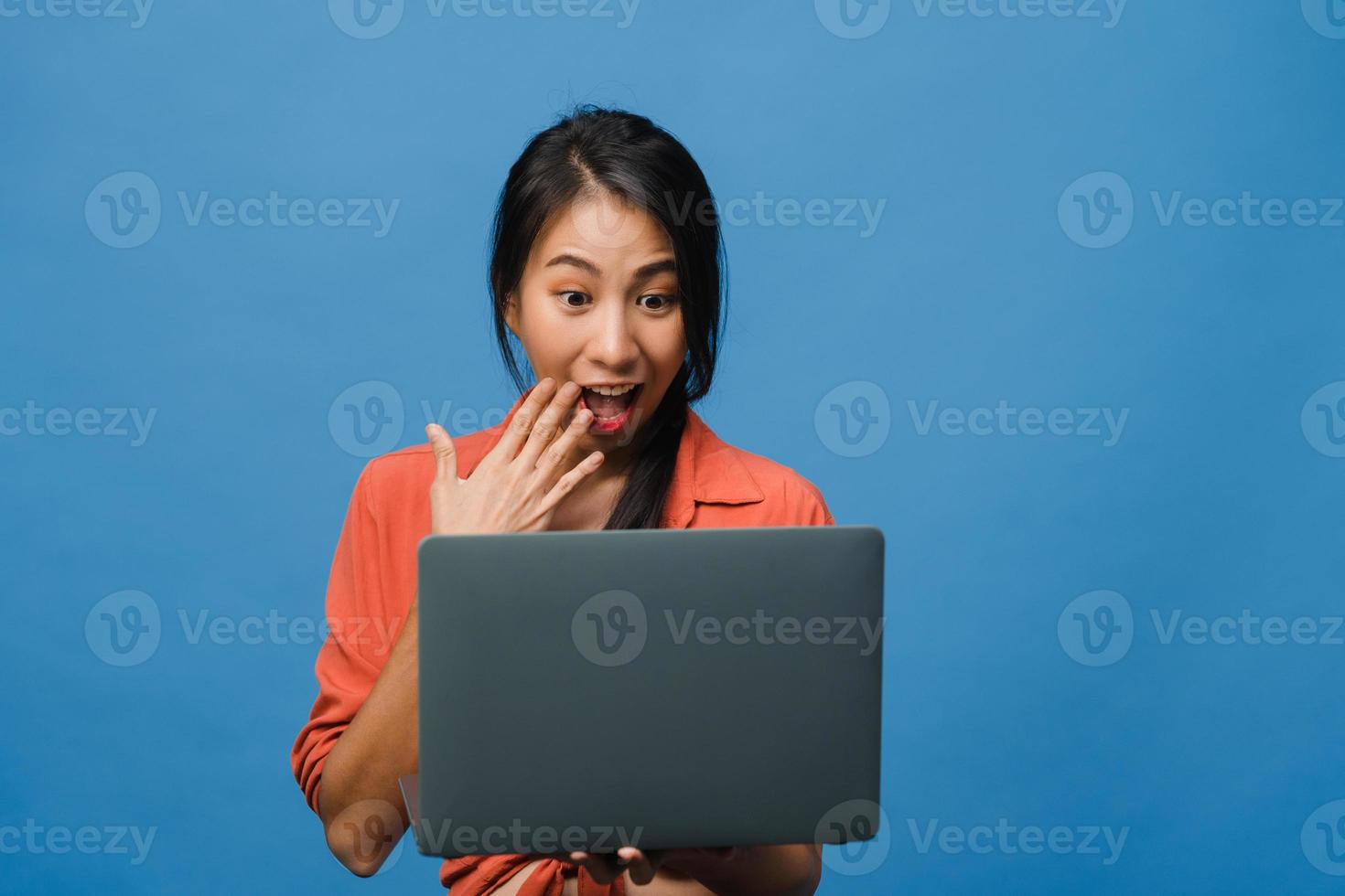 jovem asiática usando laptop com expressão positiva, sorri amplamente, vestida com roupas casuais, sentindo felicidade e carrinho isolado sobre fundo azul. feliz adorável feliz mulher alegra sucesso. foto