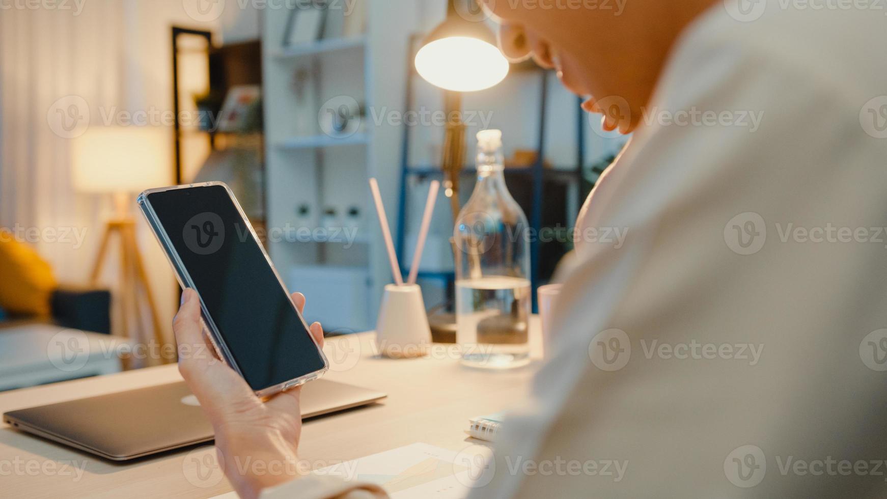 jovem senhora asiática usar telefone inteligente com simulação de tela preta em branco para texto de publicidade enquanto inteligente trabalhando em casa na sala de estar à noite. tecnologia chroma key, conceito de design de marketing. foto