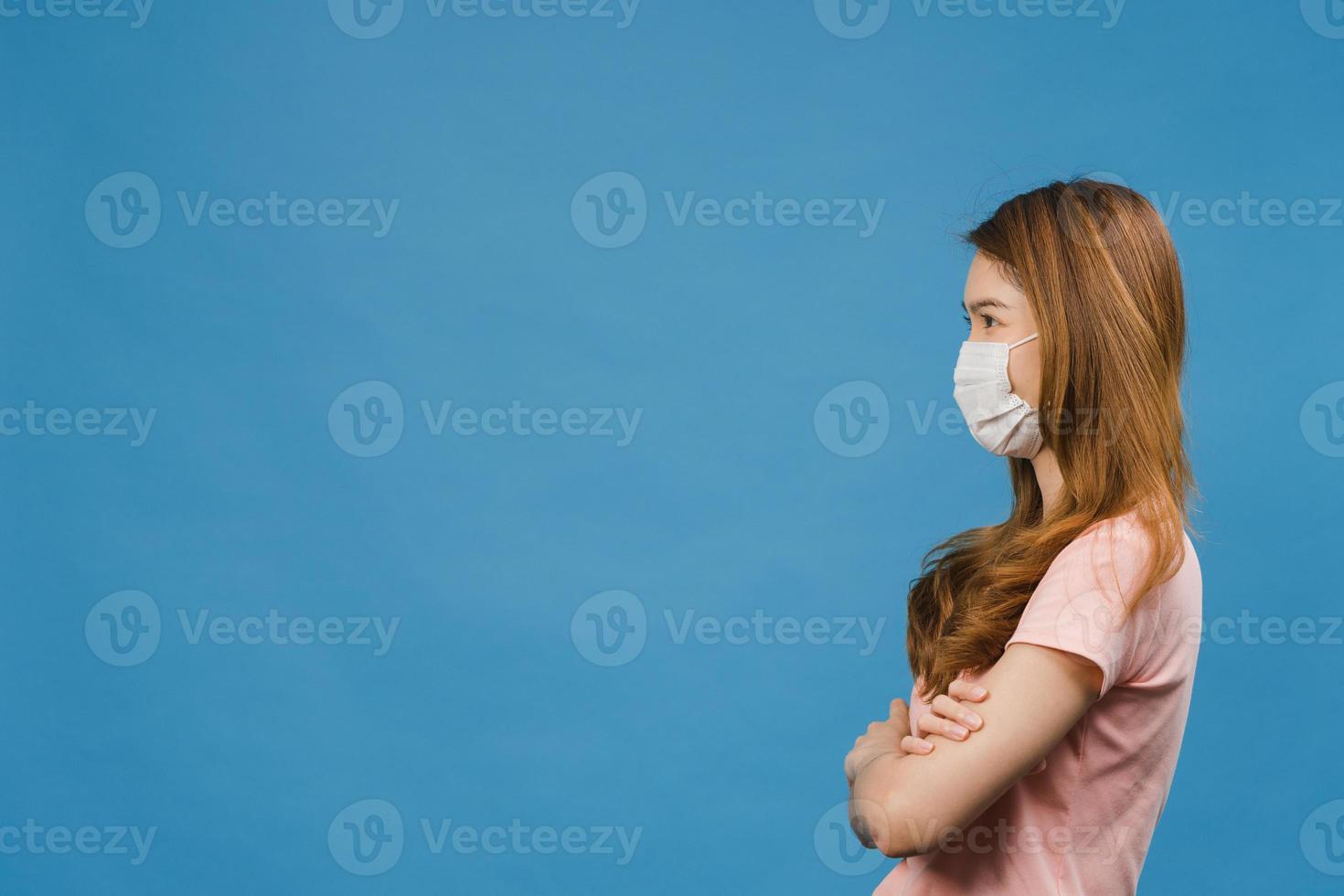 jovem asiática usando máscara médica com vestido de pano casual e olhando para o espaço em branco isolado sobre fundo azul. auto-isolamento, distanciamento social, quarentena para prevenção do vírus corona foto