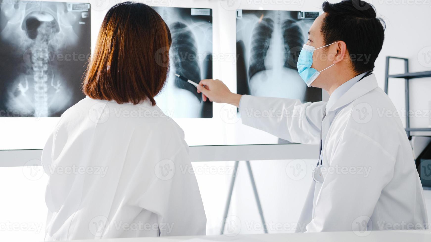 equipe médica da Ásia sério médico masculino e jovem com máscaras protetoras, discutindo o resultado da tomografia computadorizada no consultório do hospital. distância social, estilo de vida novo normal após o vírus corona. foto