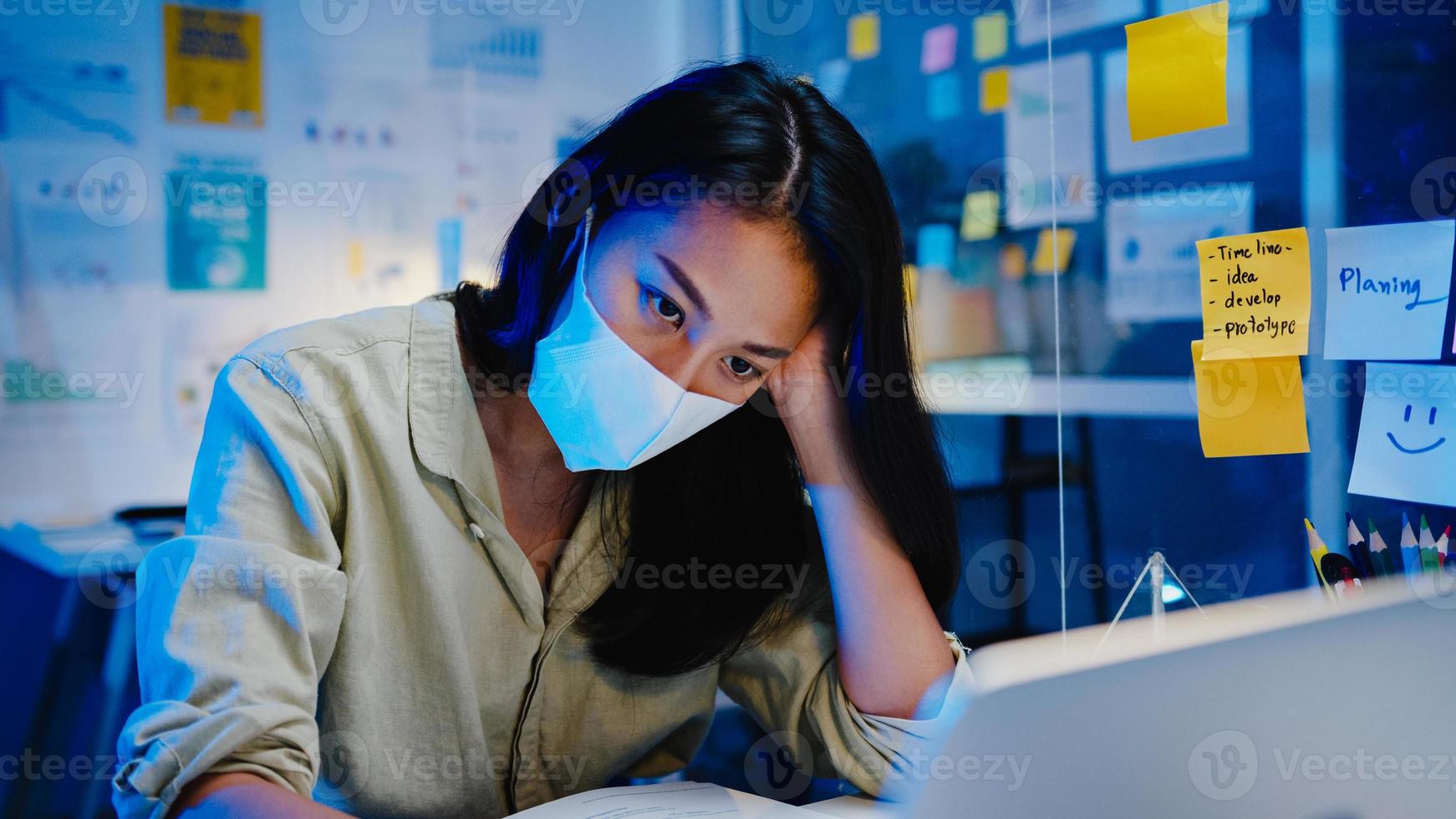 mulheres asiáticas freelance usam máscara facial usando trabalho duro do laptop no novo escritório normal. sobrecarga noturna de trabalho em casa, auto-isolamento, distanciamento social, quarentena para prevenção do vírus corona. foto