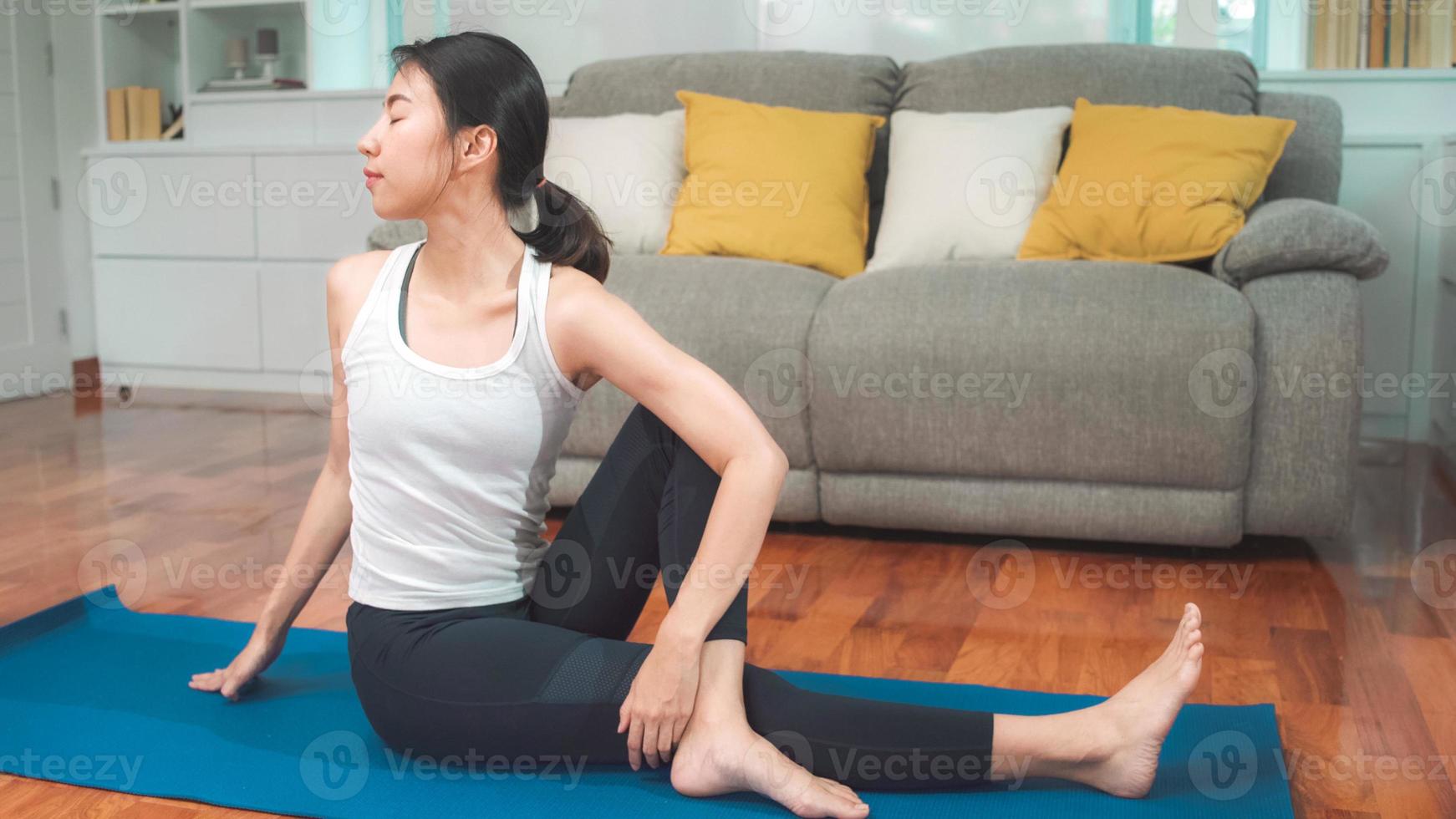 jovem mulher asiática praticando ioga na sala de estar. atraente mulher bonita malhando para uma saúde saudável em casa. conceito de exercício de mulher de estilo de vida. foto