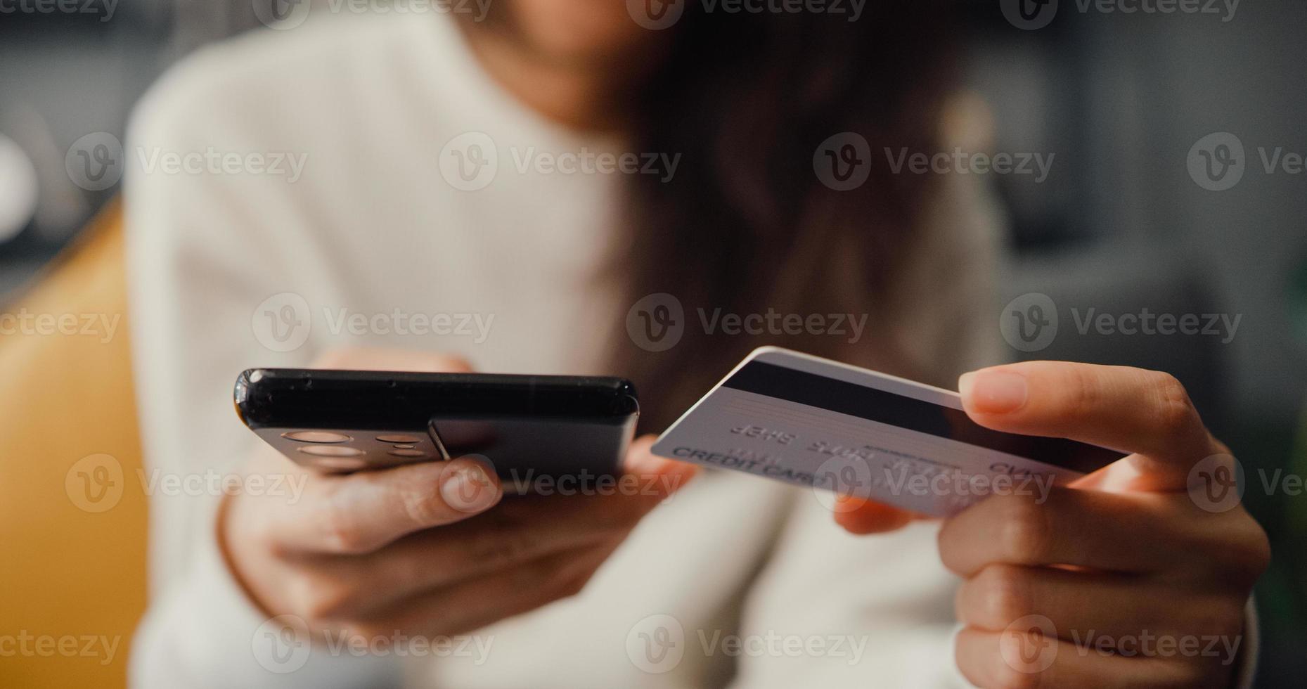 closeup jovem senhora asiática usar um produto de compra on-line de pedido de celular e pagar contas com cartão de crédito, sentar no sofá na sala de estar em casa, atividade de quarentena, atividade divertida para a prevenção do coronavírus. foto