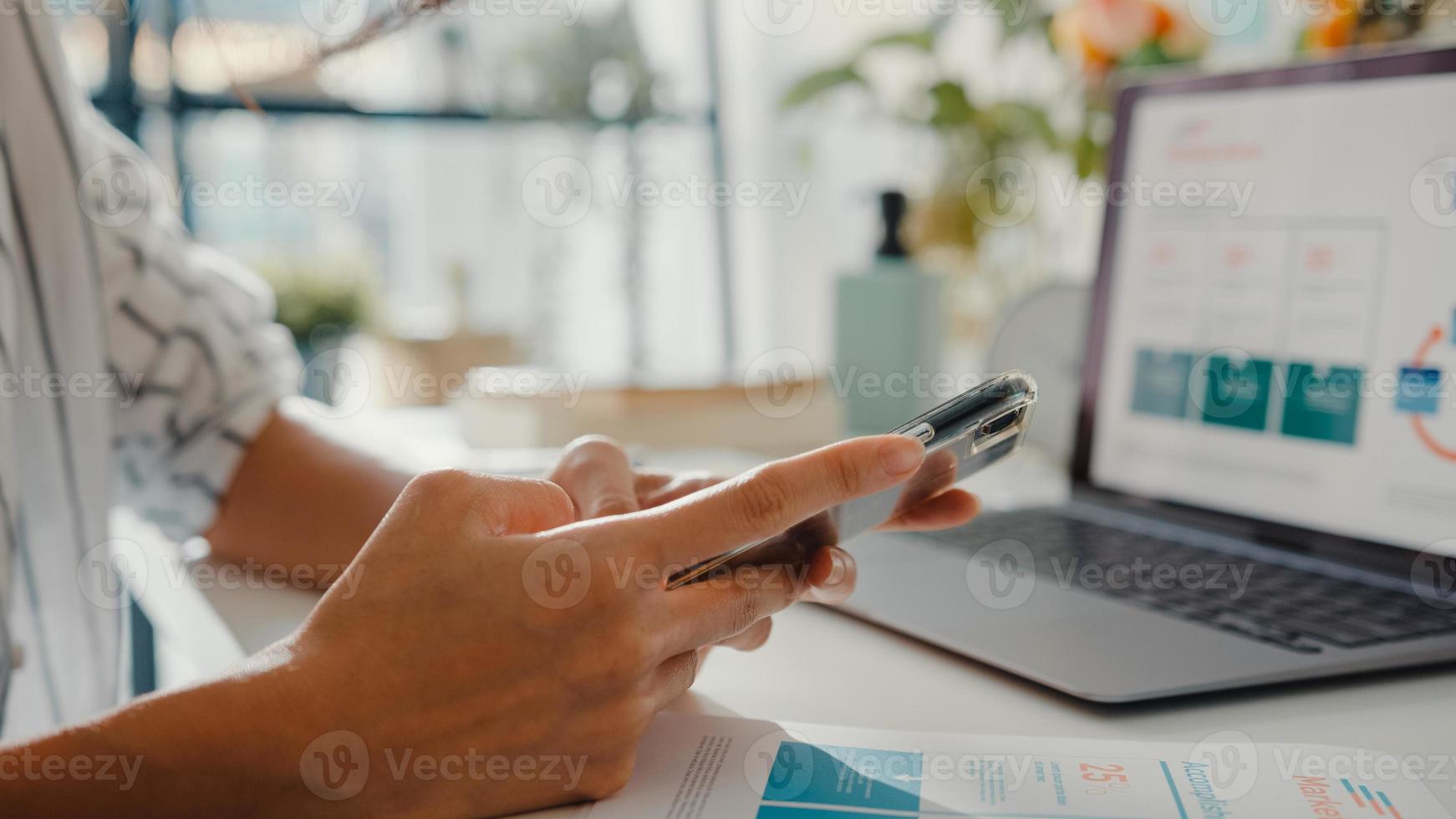 close-up jovem ásia freelance foco móvel bate-papo com colegas trabalho finanças gráfico conta gráfico plano de mercado no laptop em casa. aluna aprender online em casa, trabalhar a partir do conceito de casa. foto