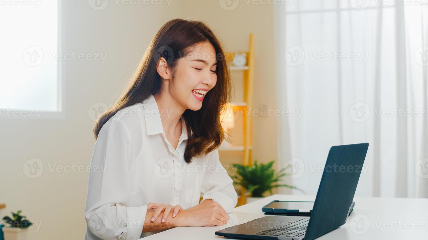 mulher de negócios asiáticos jovem usando videochamada de laptop falando com o casal enquanto trabalhava em casa na sala de estar. auto-isolamento, distanciamento social, quarentena para coronavírus no próximo conceito normal. foto