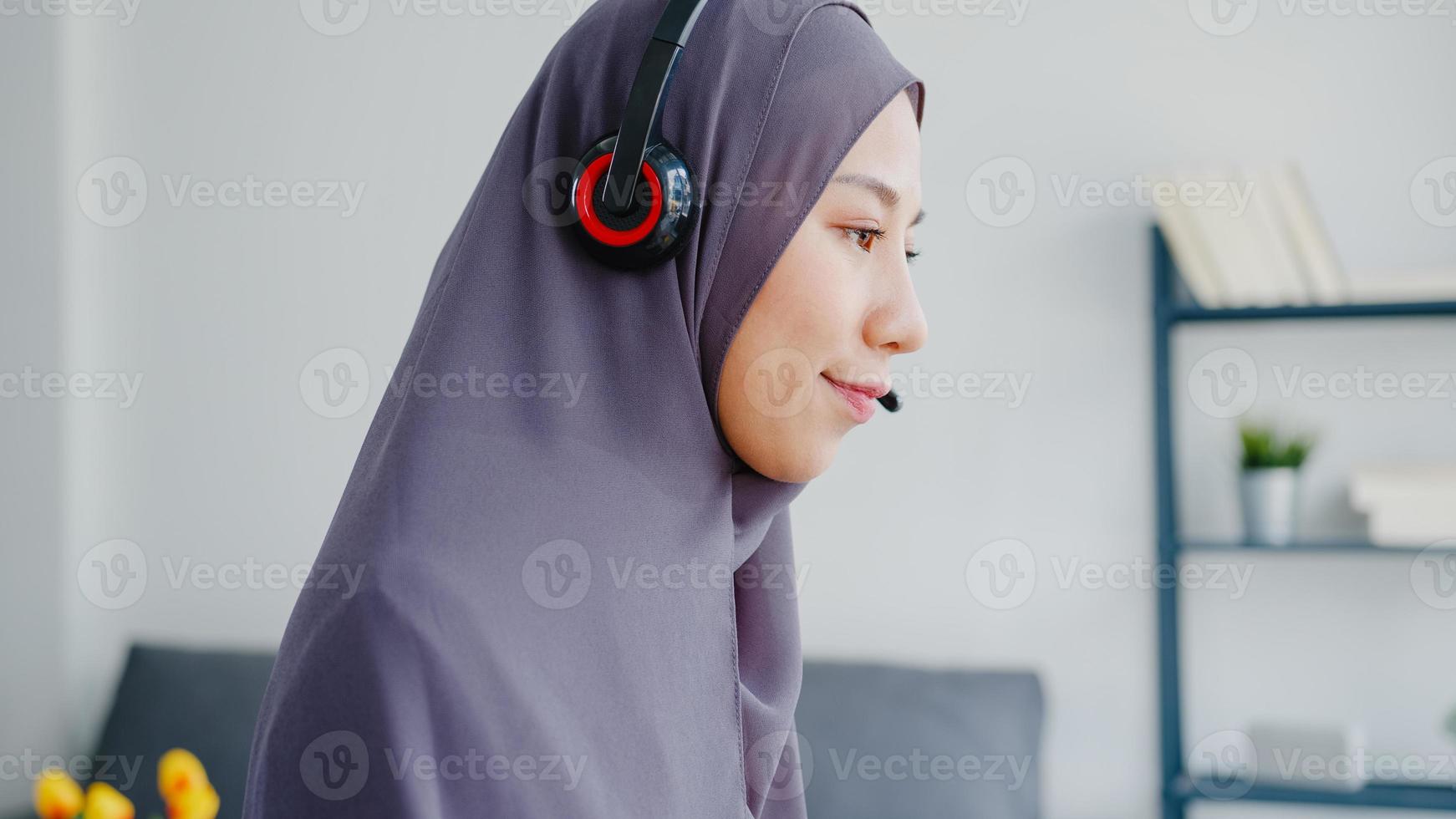 ásia senhora muçulmana usar fone de ouvido assistir webinar ouvir curso on-line comunicar-se por videoconferência em casa. trabalho remoto de casa, distanciamento social, quarentena para prevenção do vírus corona. foto