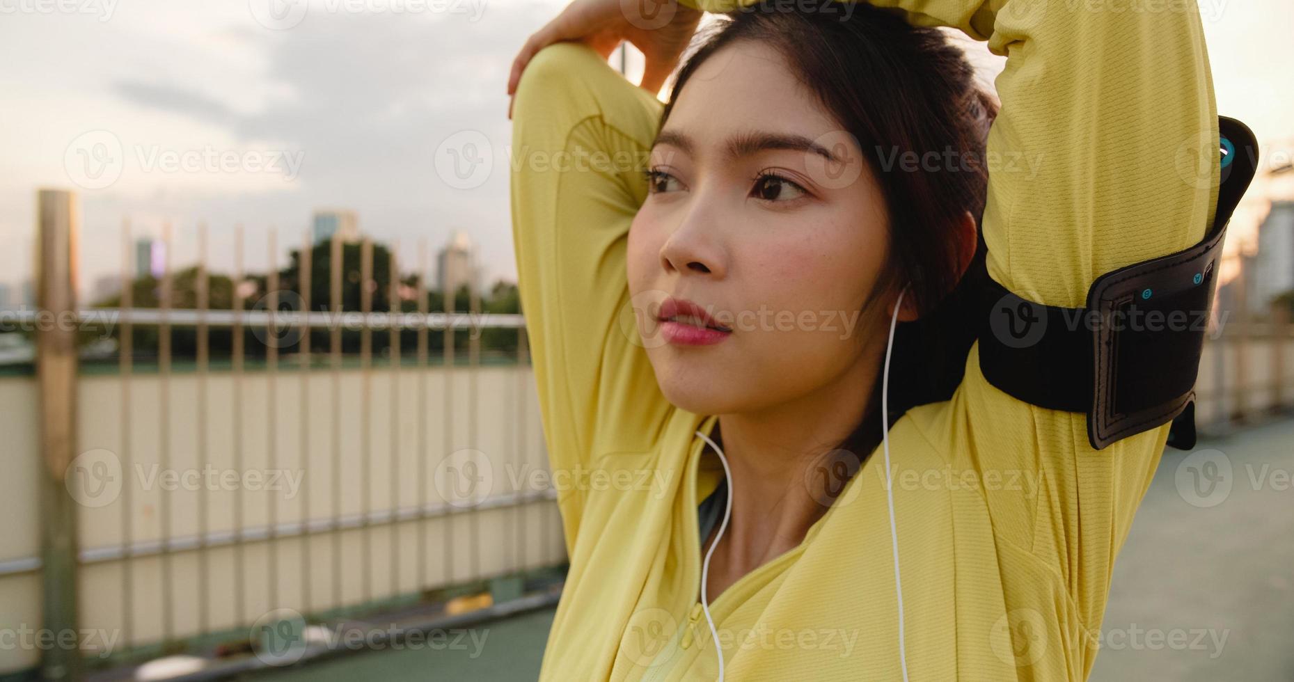 bela jovem atleta da Ásia exercícios usando smartphone para ouvir música enquanto corre em ambiente urbano. adolescente coreana vestindo roupas esportivas na ponte de passagem no início da manhã. foto