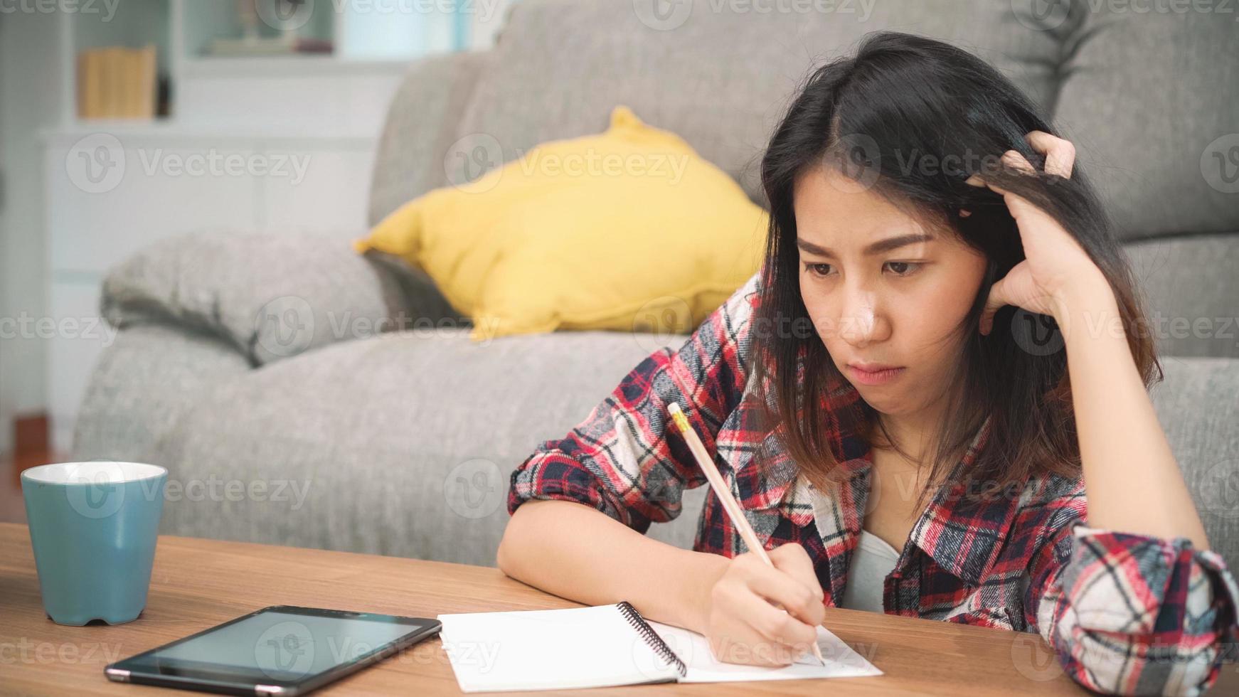 mulher estudante asiática fazer lição de casa em casa, mulher usando tablet para pesquisar no sofá na sala de estar em casa. mulheres de estilo de vida relaxam no conceito de casa. foto