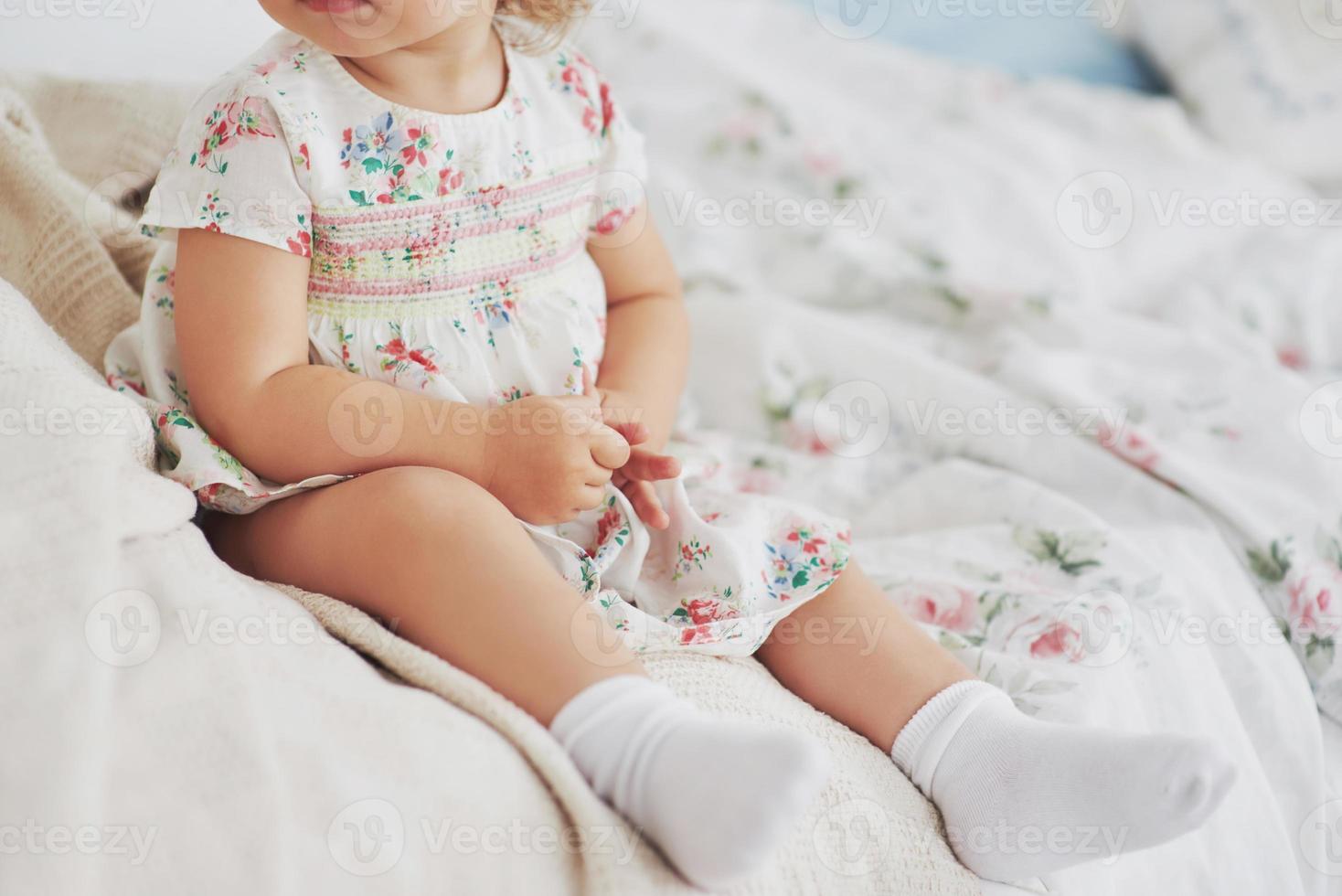 conceito de infância. menina com vestido bonito localização na cama brincando com brinquedos em casa. quarto infantil branco vintage foto