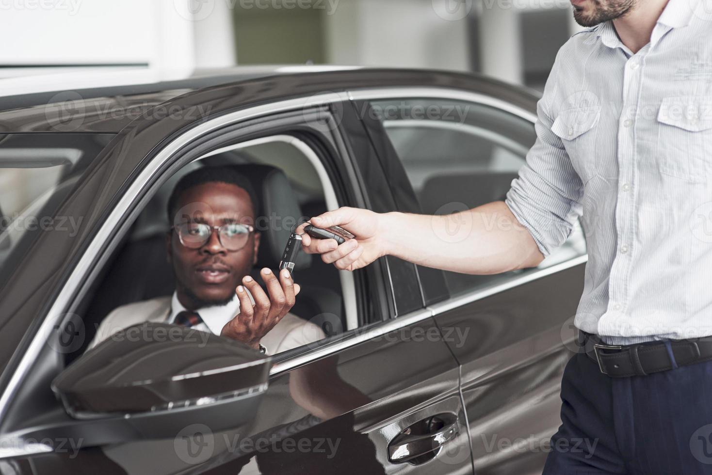 um afro-americano pega as chaves de um carro em uma concessionária. foto