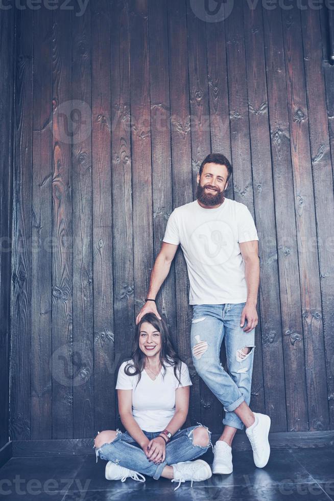 jovem casal, cara e garota juntos em um fundo de parede de madeira. eles são felizes juntos e vestidos da mesma forma. sempre em tendência foto