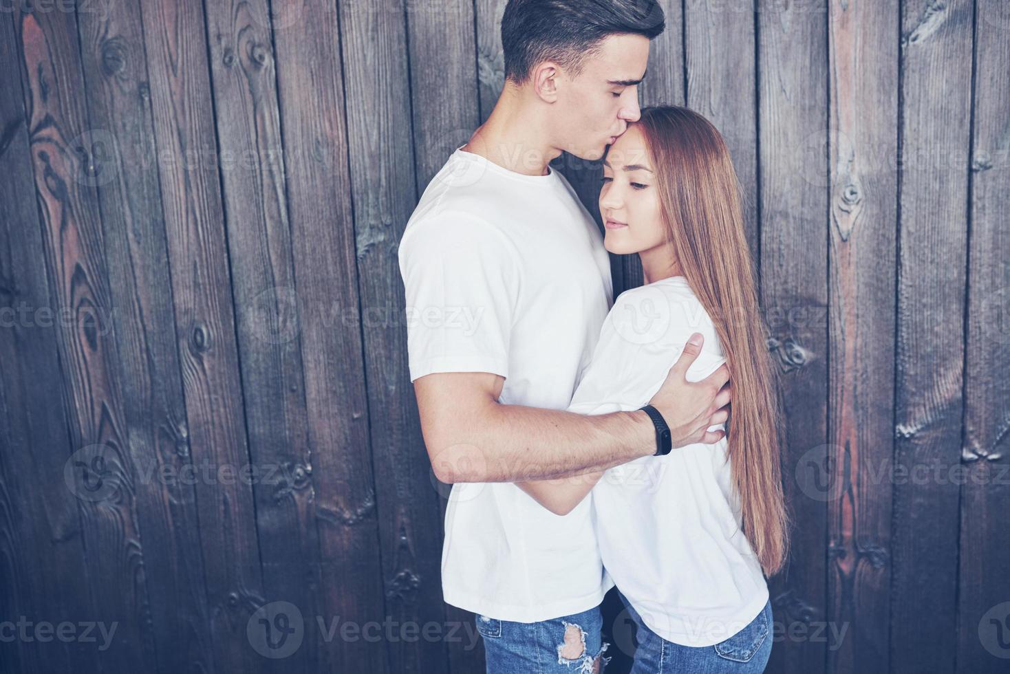 jovem casal, cara e garota juntos em um fundo de parede de madeira. eles são felizes juntos e vestidos da mesma forma. sempre em tendência foto