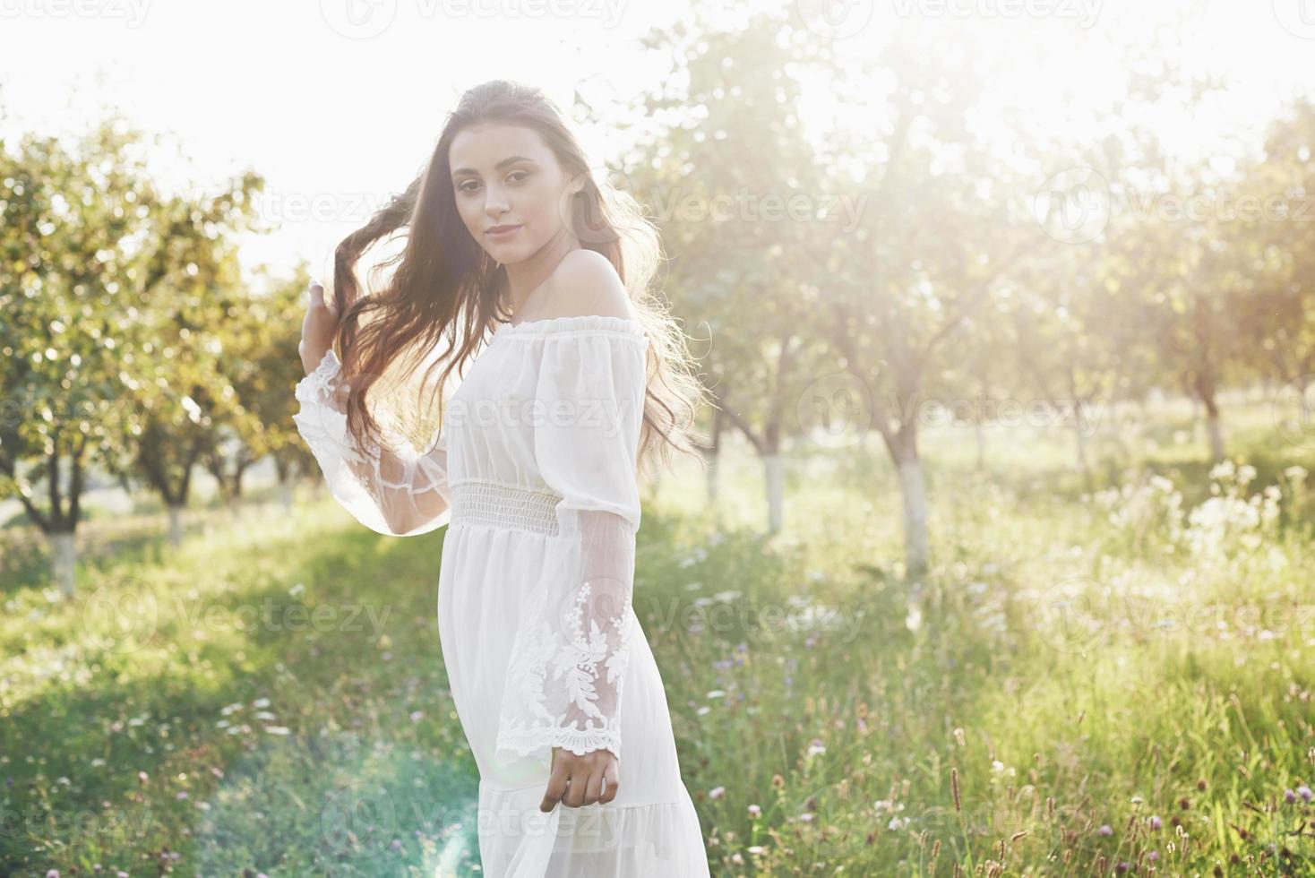 bela jovem usando um vestido branco elegante e curtindo uma bela tarde de sol em um jardim de verão foto