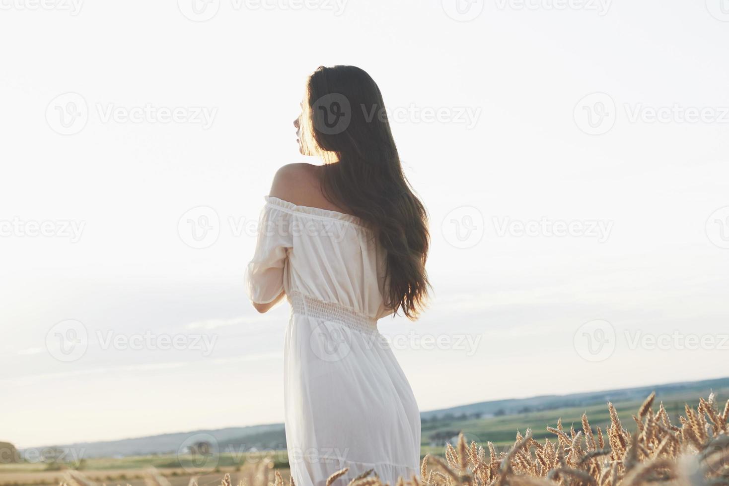 linda garota de vestido branco correndo no campo de trigo de outono ao pôr do sol foto