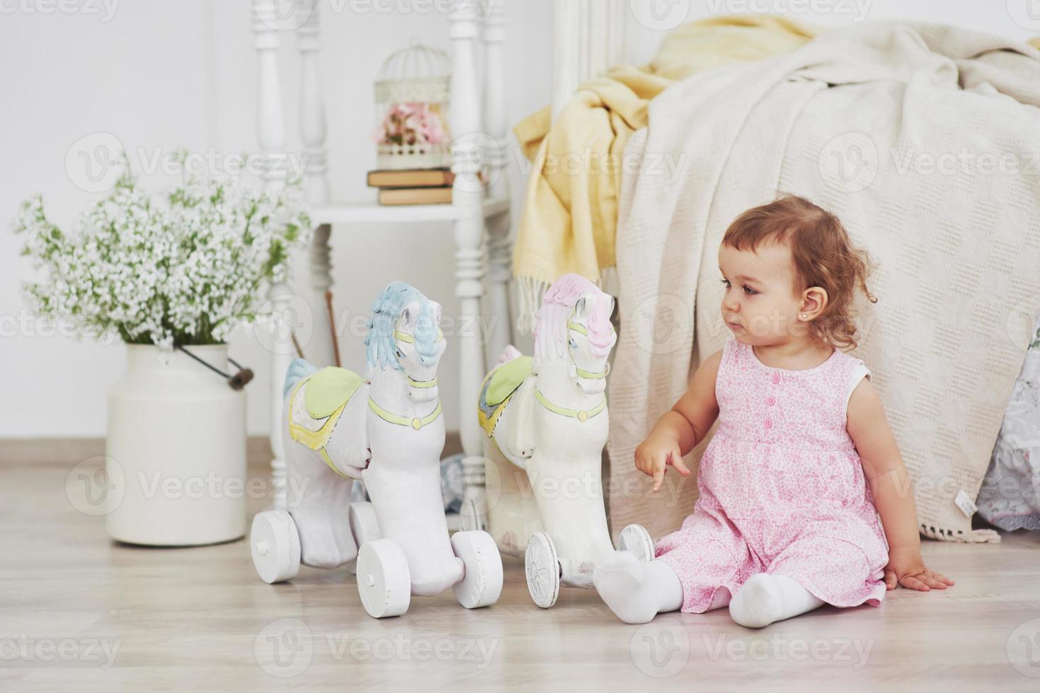 linda garotinha brincando de brinquedos. loira de olhos azuis. cadeira branca. quarto das crianças. retrato de menina feliz. conceito de infância foto