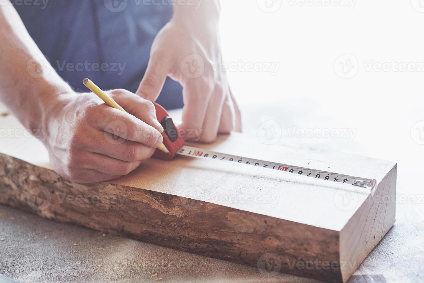 um carpinteiro com roupa de trabalho e um pequeno empresário pegam uma placa de madeira com uma régua e um lápis. foto