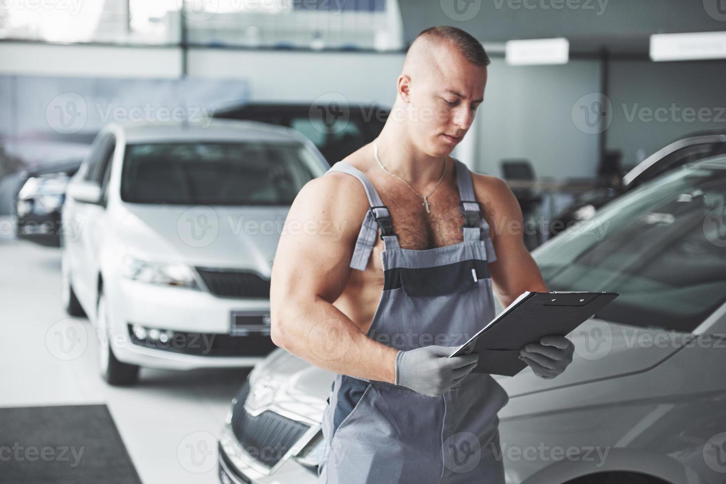 um jovem bonito fala em uma concessionária de automóveis, consertando um carro em uma oficina. foto