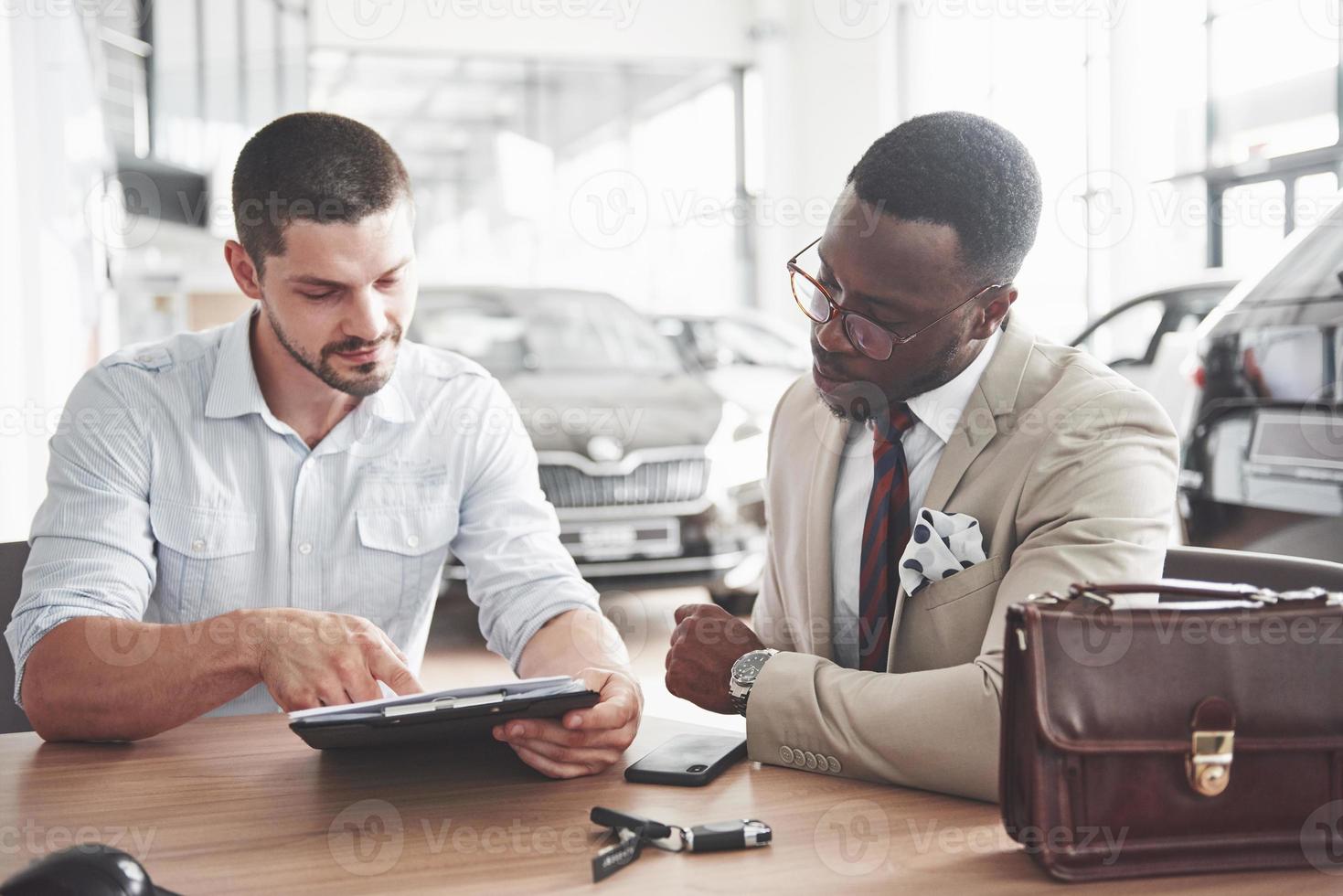 um jovem empresário negro e atraente compra um carro novo, assina um contrato e leva as chaves ao gerente foto