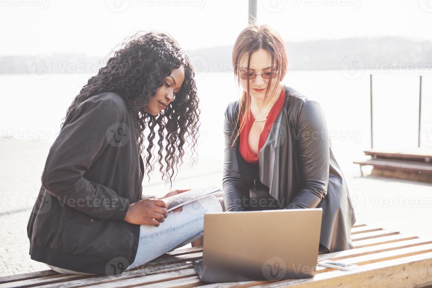 dois lindos blogueiros multiétnicos estão usando a Internet ao ar livre com seus laptops foto