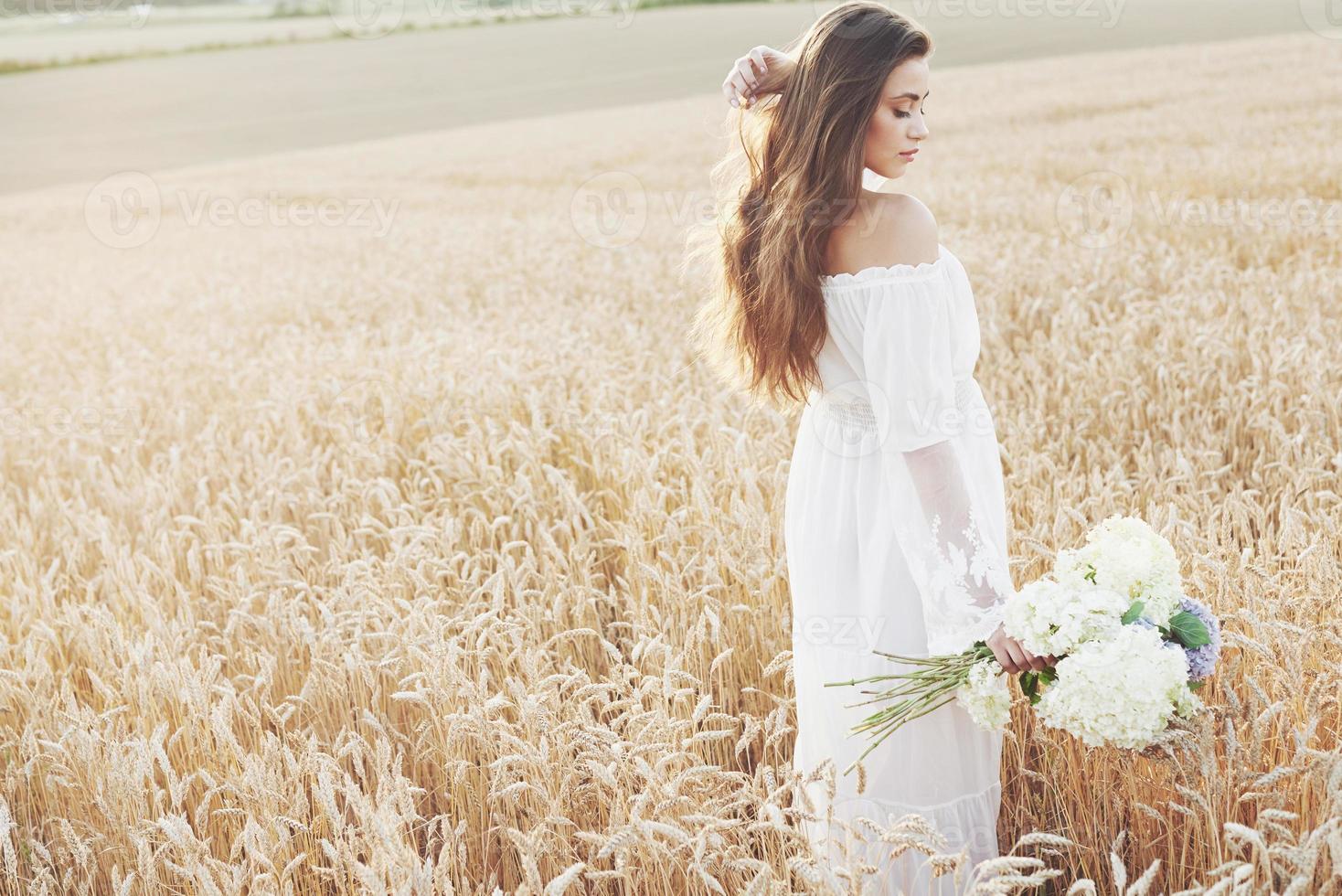 linda garota de vestido branco correndo no campo de trigo de outono ao pôr do sol foto