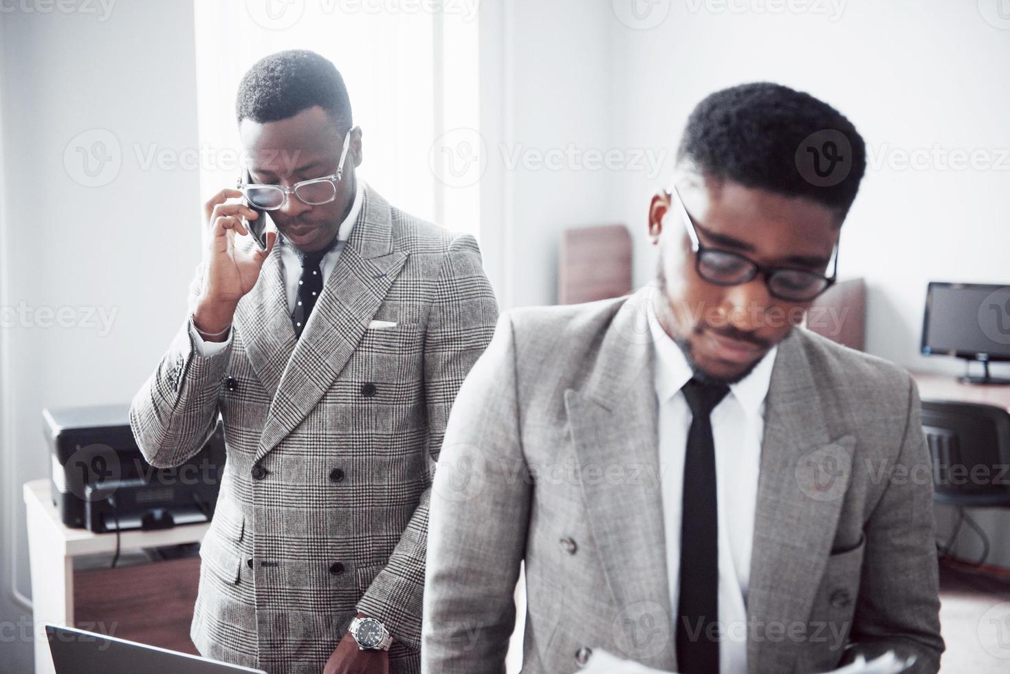 empresário moderno no trabalho. dois empresários confiantes em trajes formais discutindo algo enquanto um deles olha os documentos e o segundo uma ligação importante foto